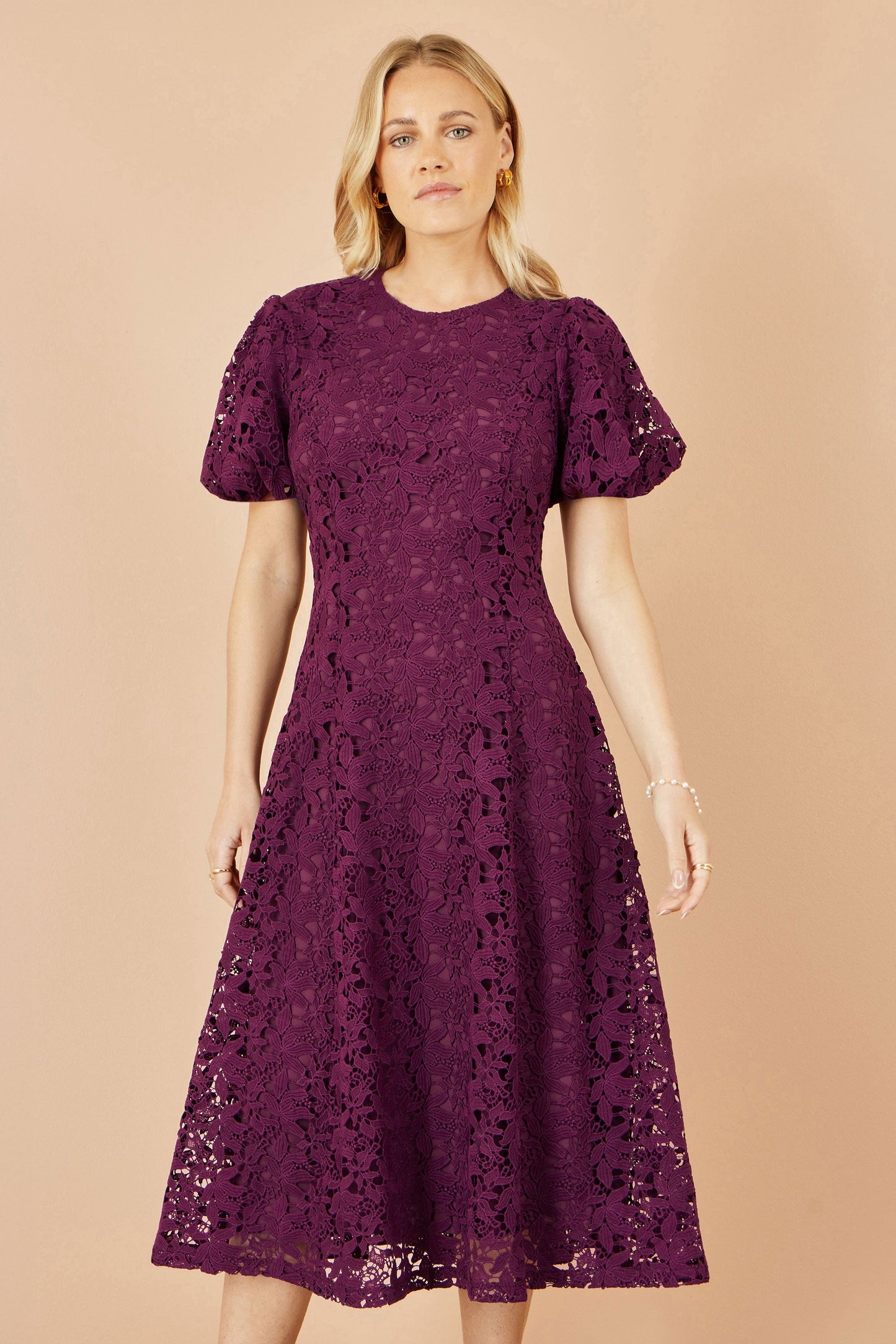 Woman wearing a purple lace dress against a beige background