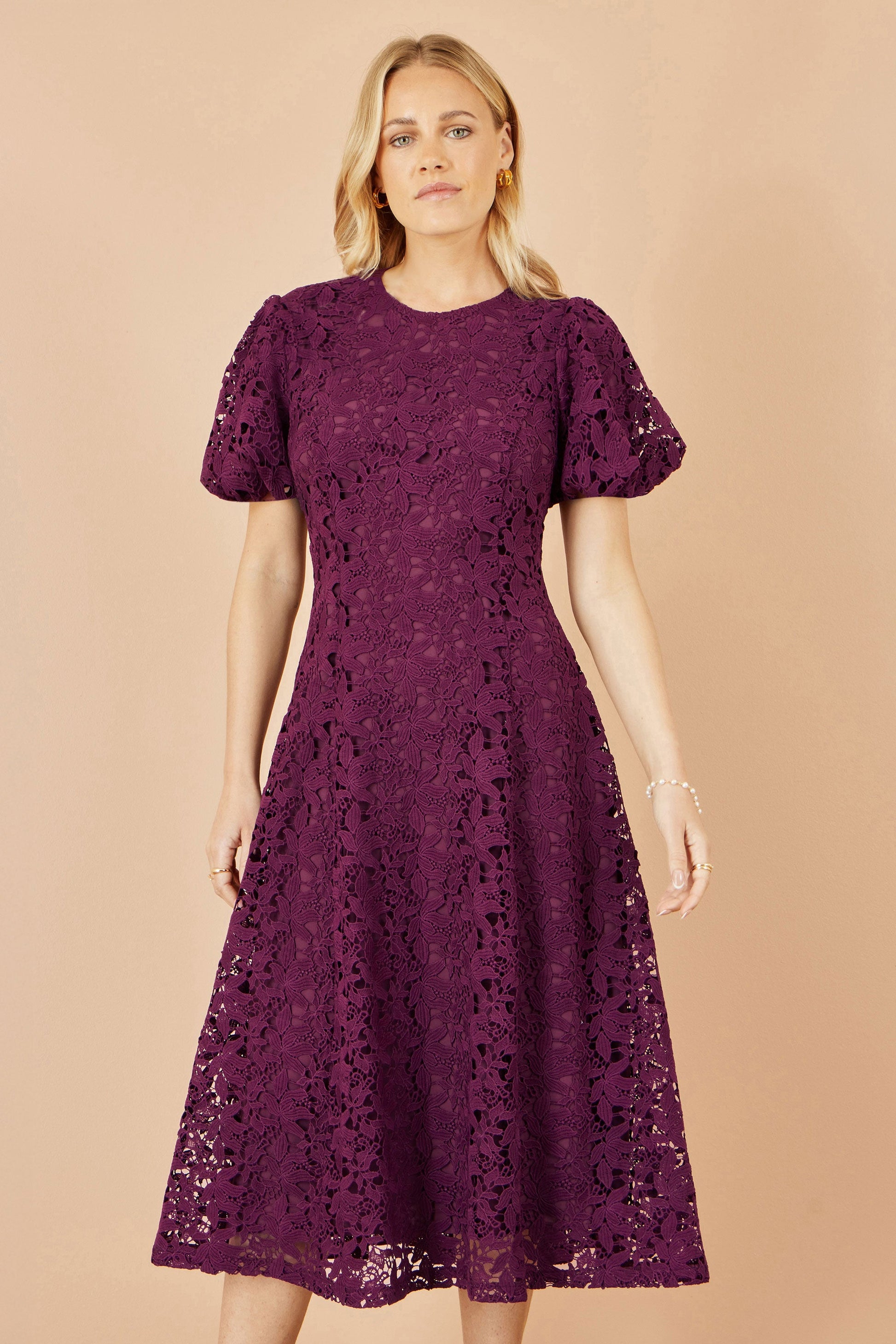 Woman wearing a purple lace dress against a beige background