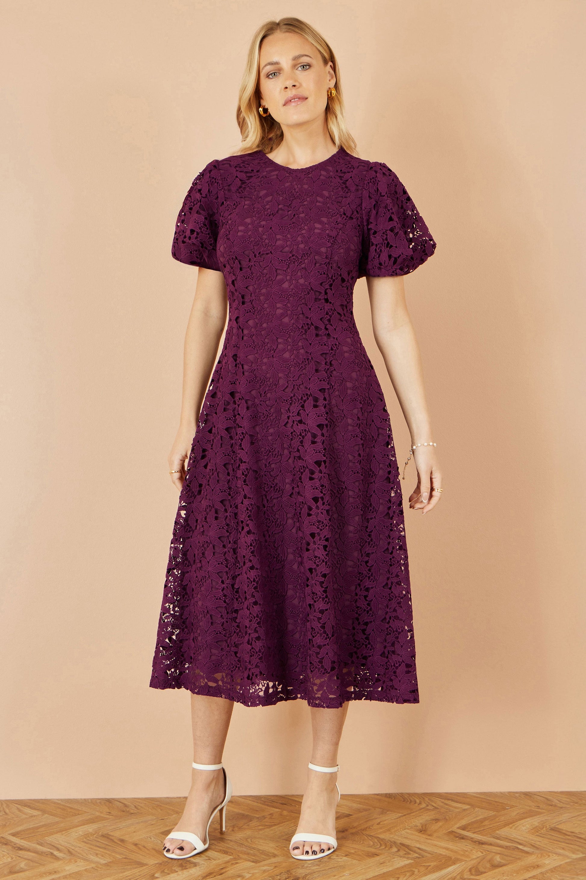 Woman wearing a purple lace dress against a beige background