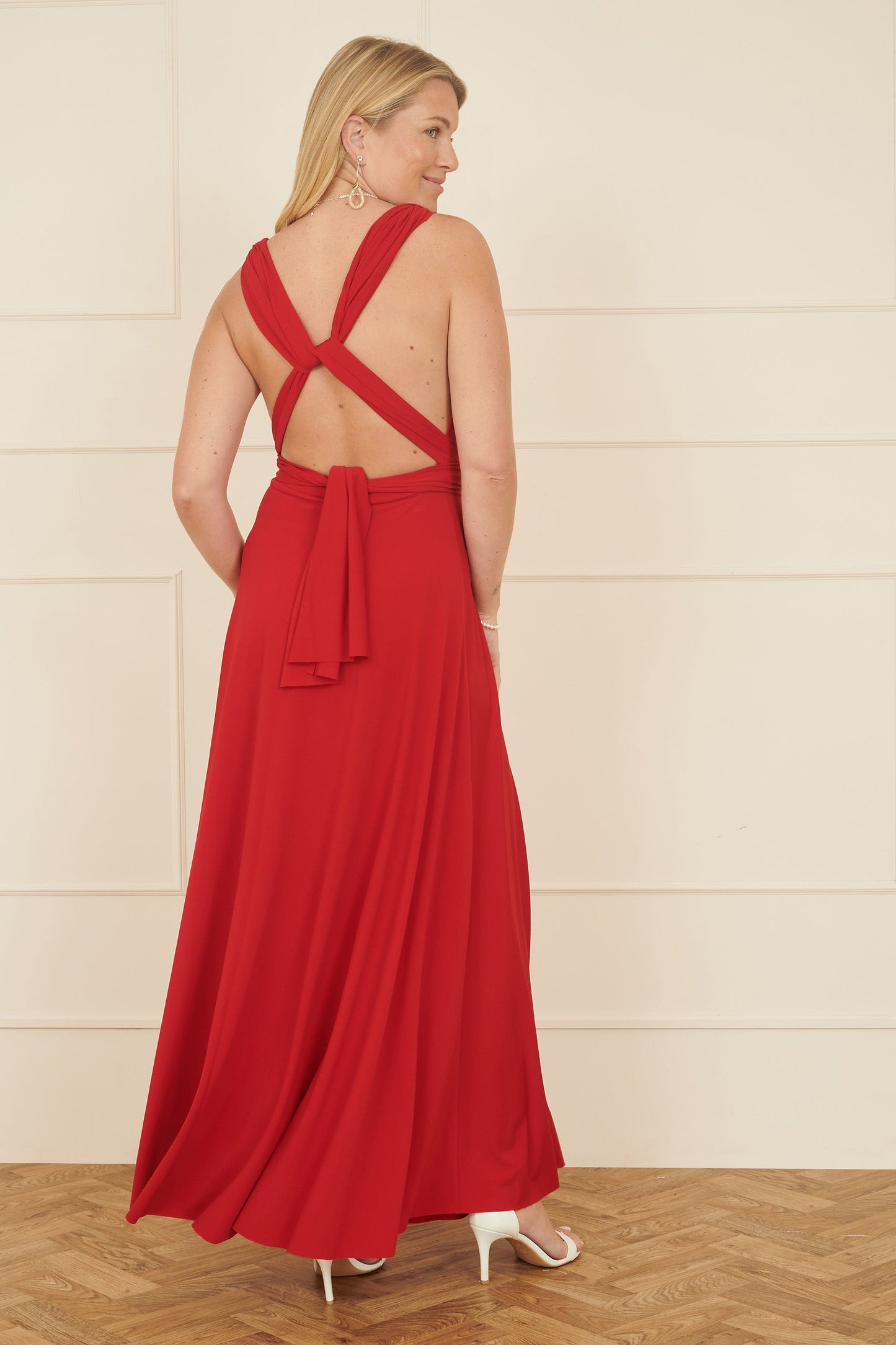 Woman wearing a red evening gown with a backless design on a wooden floor.