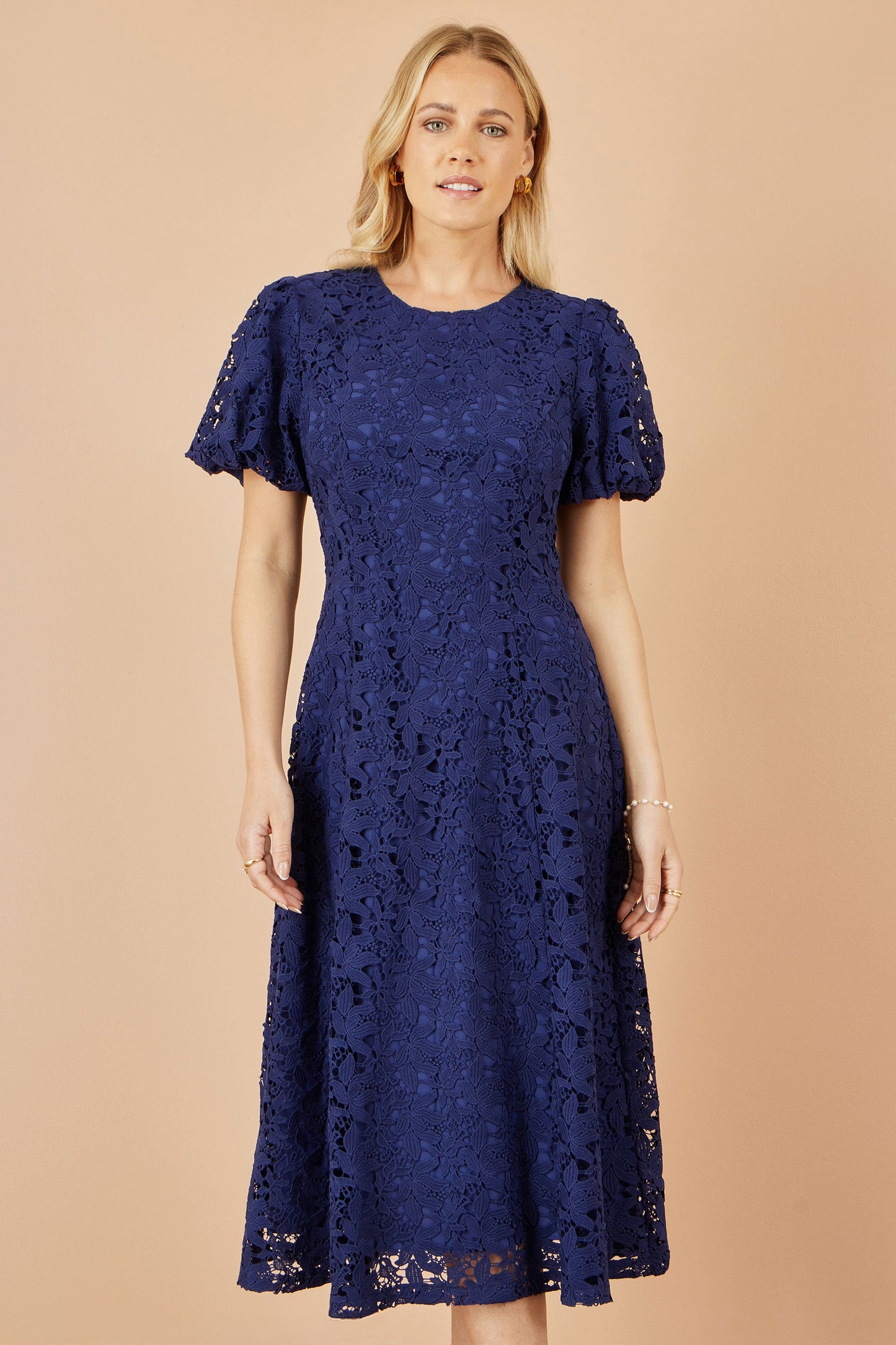 Woman wearing a navy lace dress against a beige background