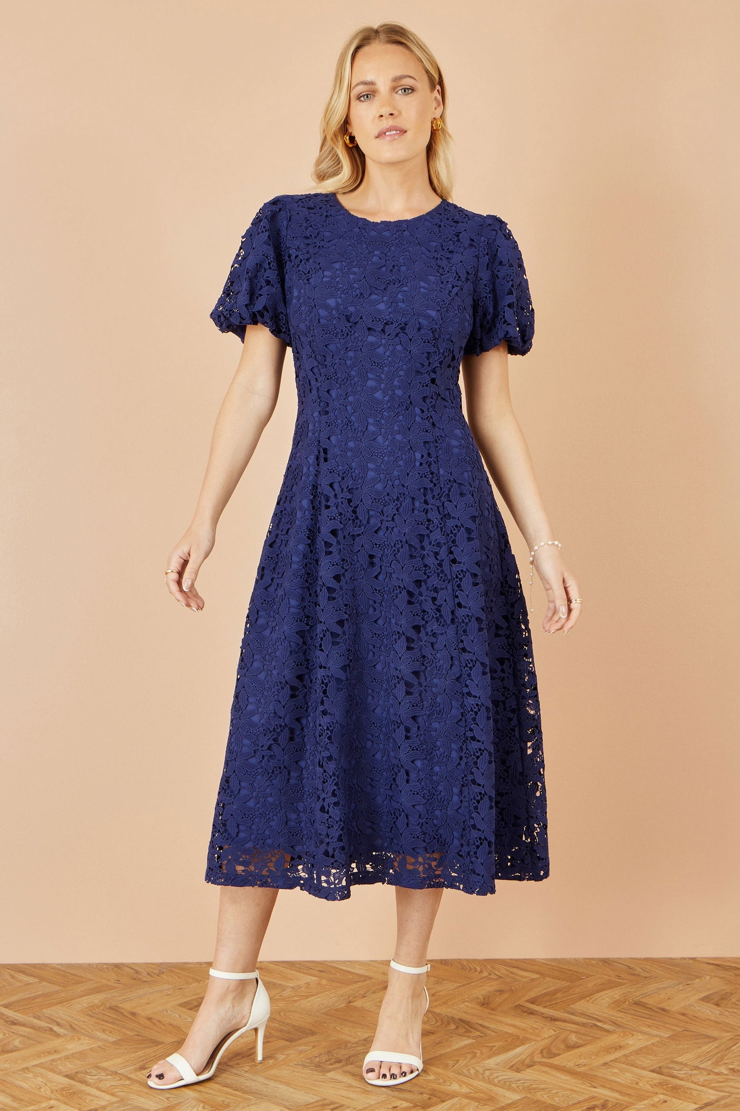 Woman wearing a navy lace dress against a beige background