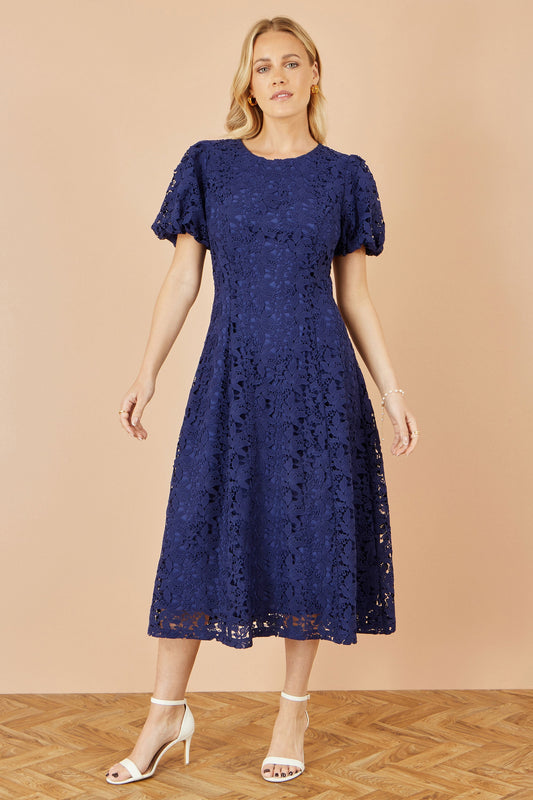 Woman wearing a navy lace dress against a beige background