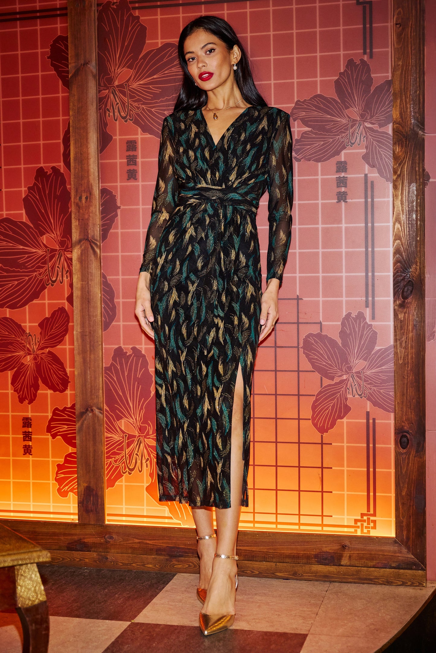 Woman in a patterned dress standing in front of a decorative wall with floral designs.