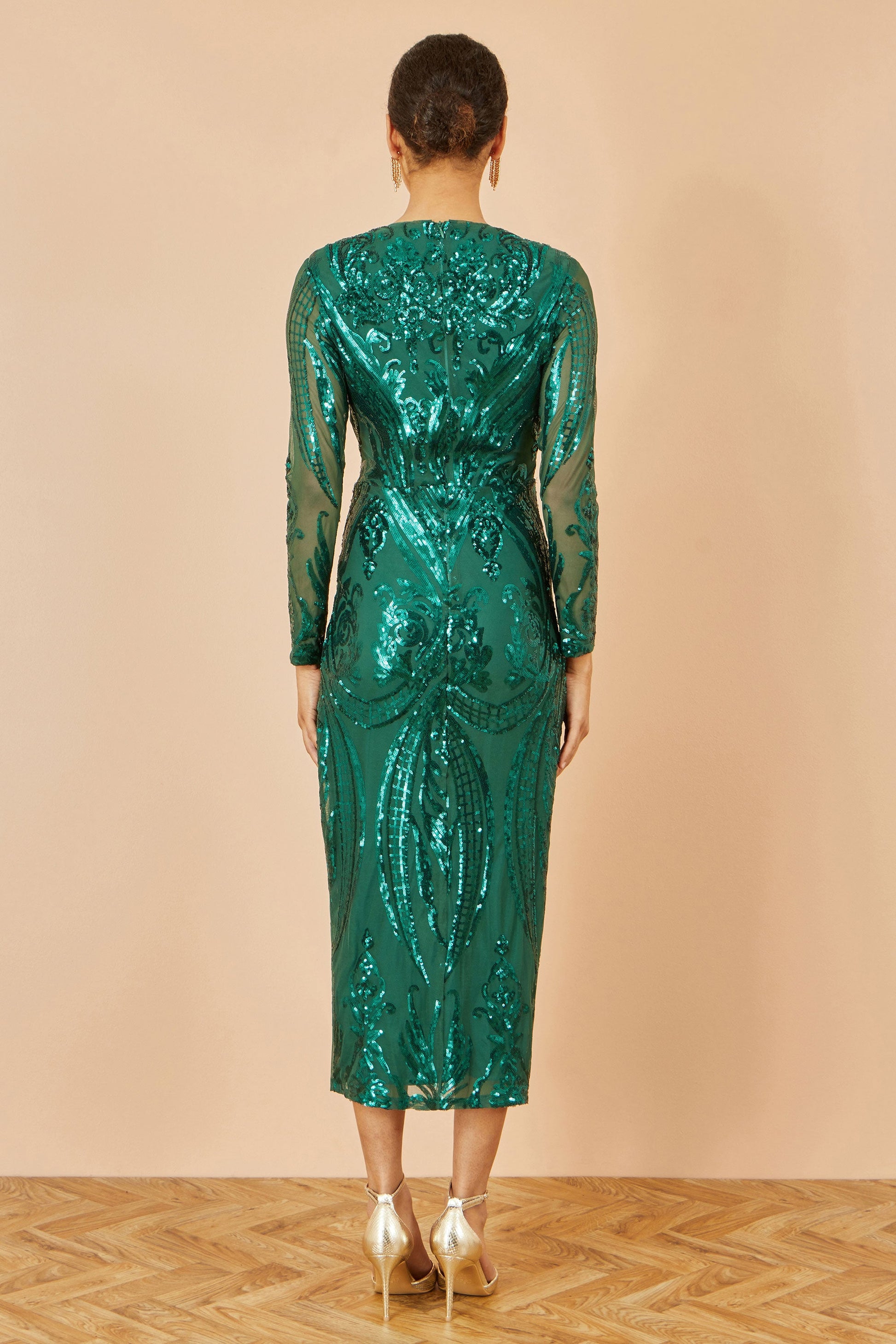 Woman wearing a green sequin dress against a beige background
