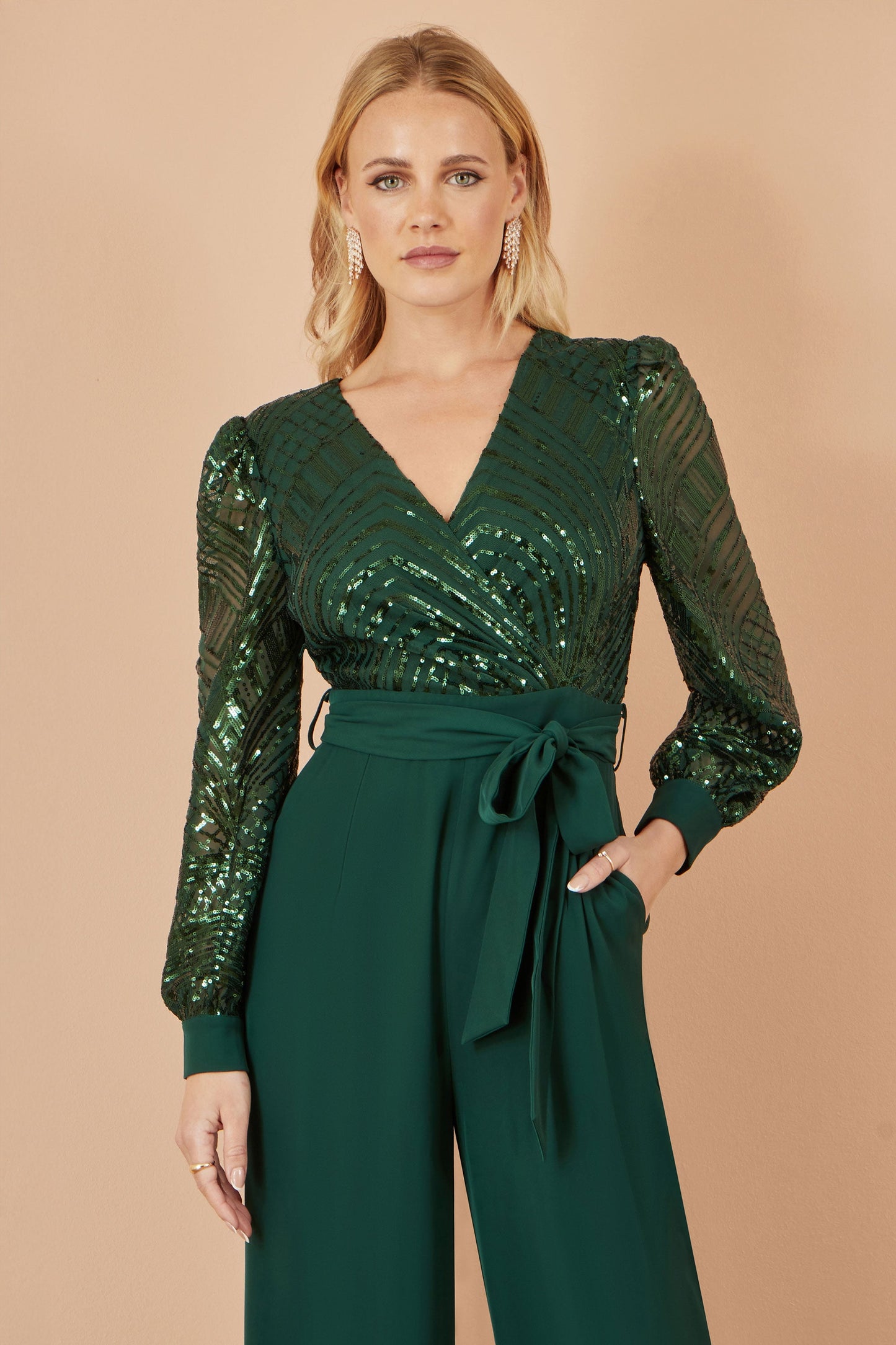Woman wearing a green sequin top and matching pants against a beige background
