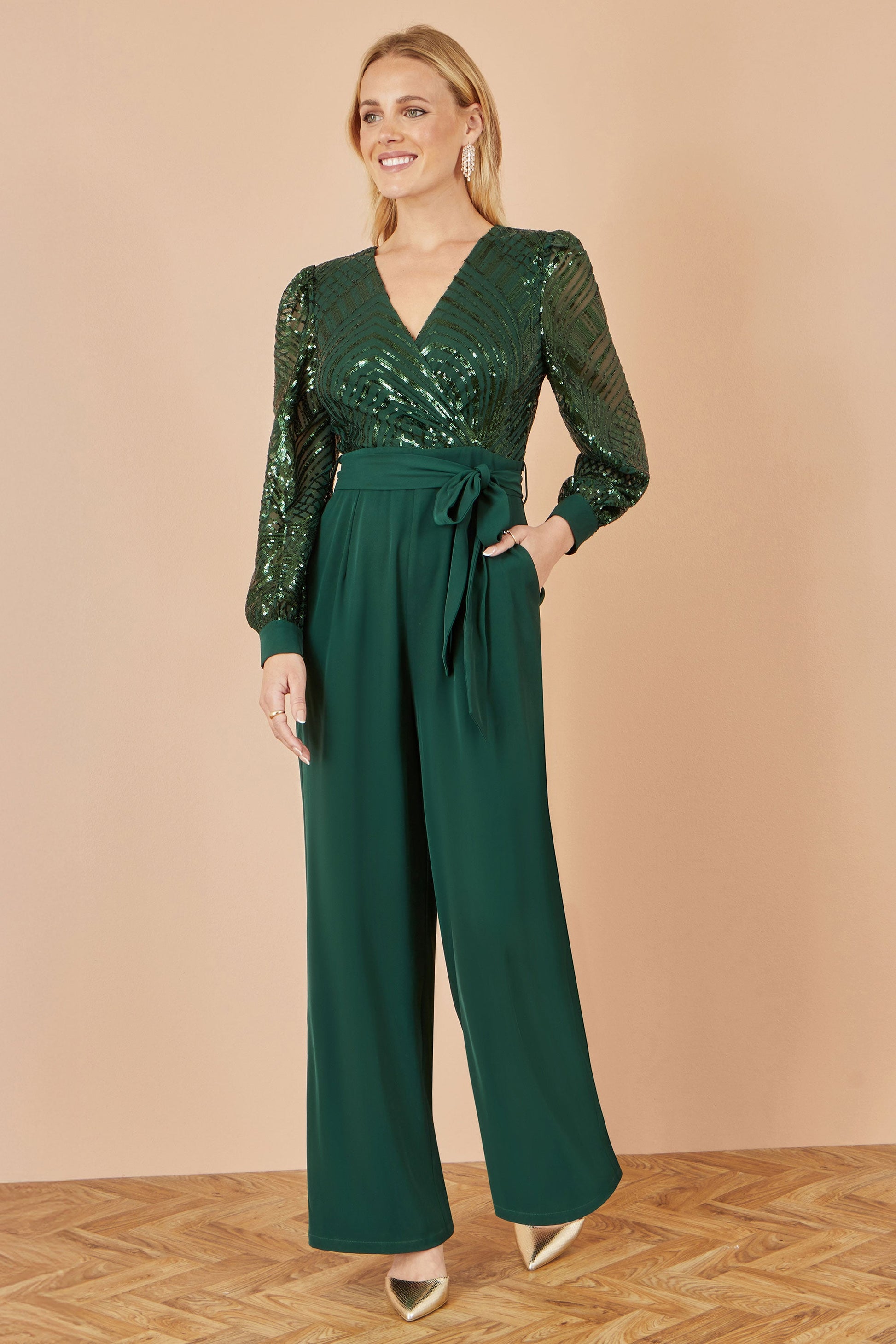 Woman wearing a green sequin jumpsuit on a beige background