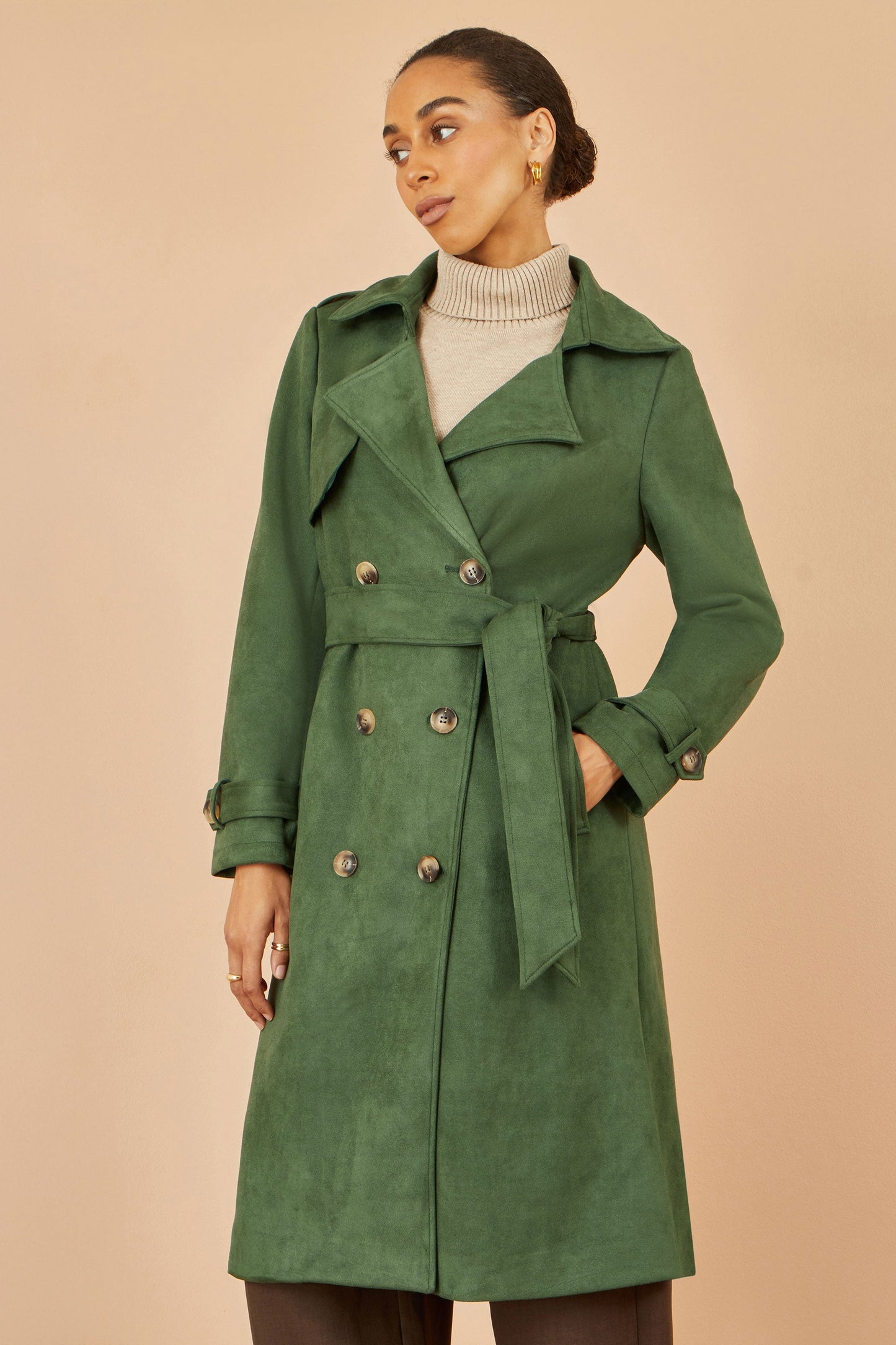 Woman wearing a green trench coat against a beige background