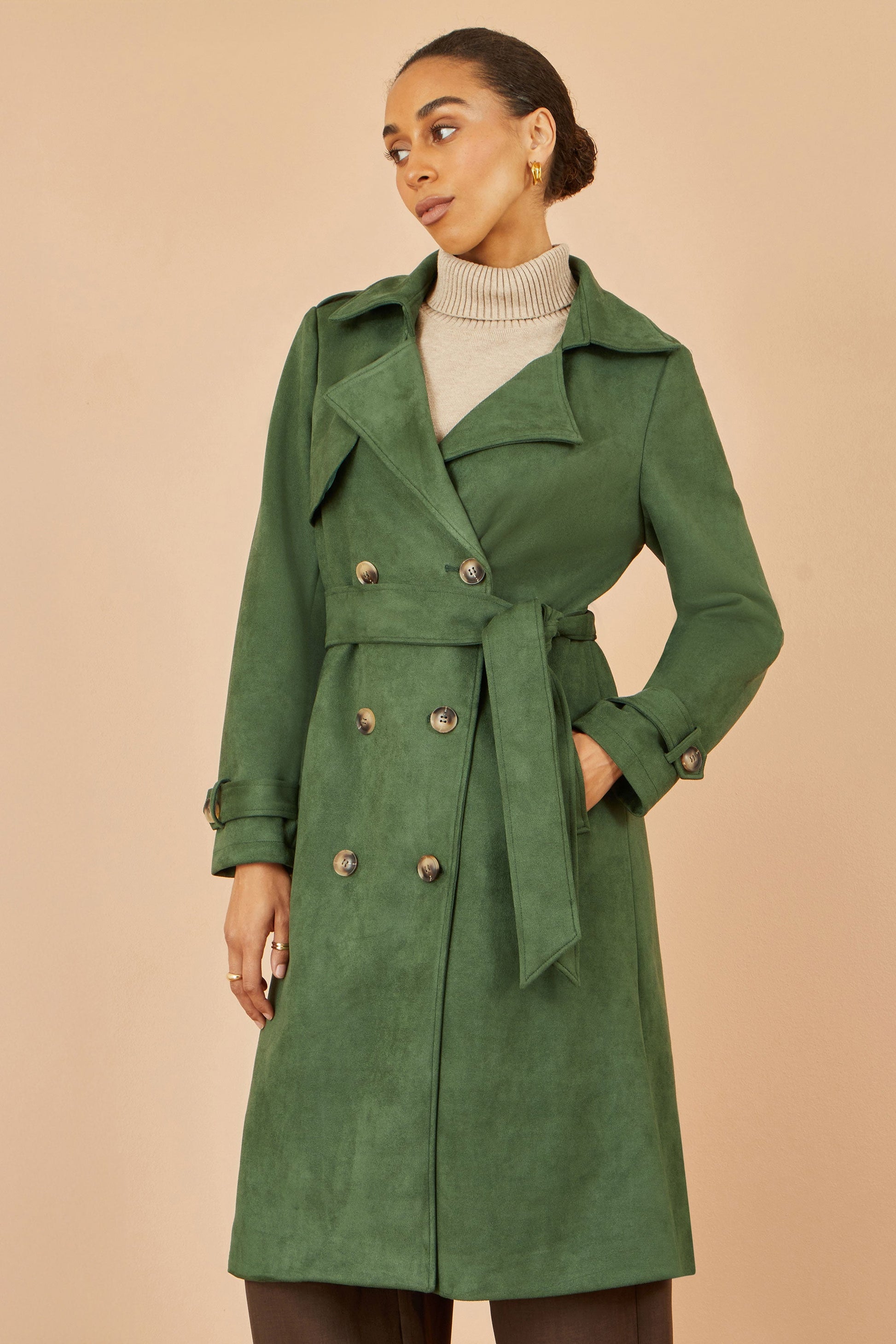 Woman wearing a green trench coat against a beige background