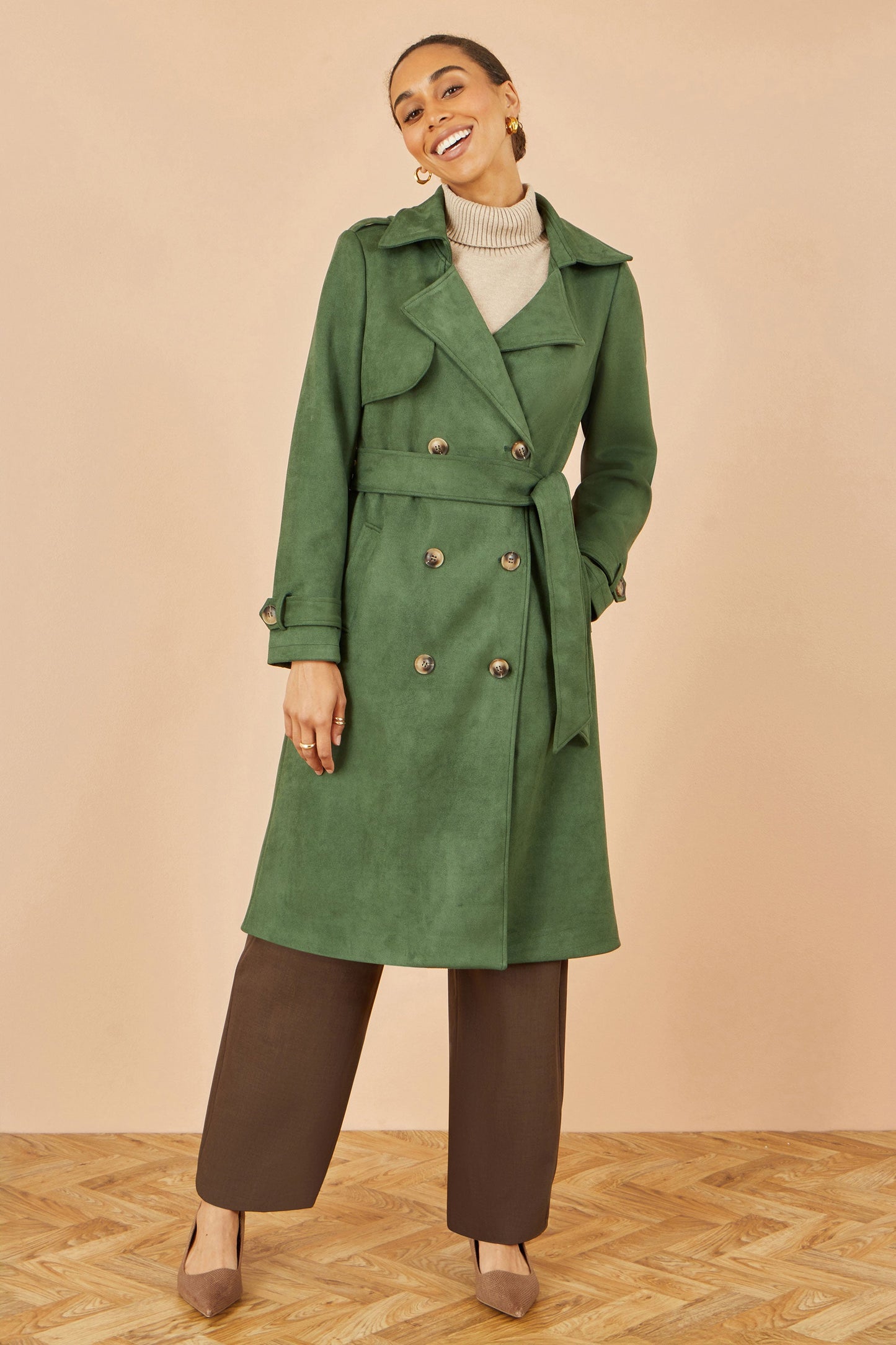 Woman wearing a green trench coat against a beige background