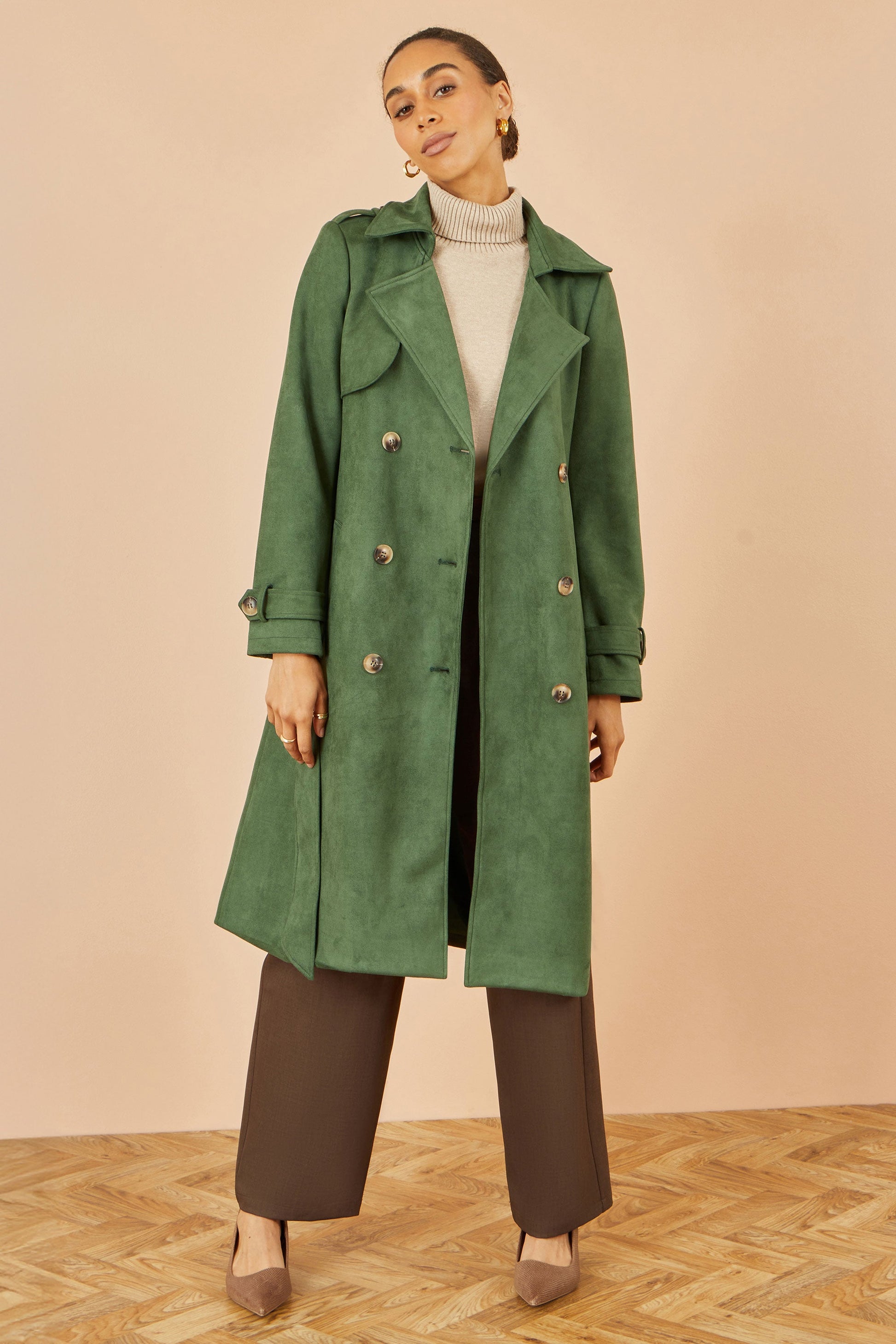 Woman wearing a green trench coat against a beige background