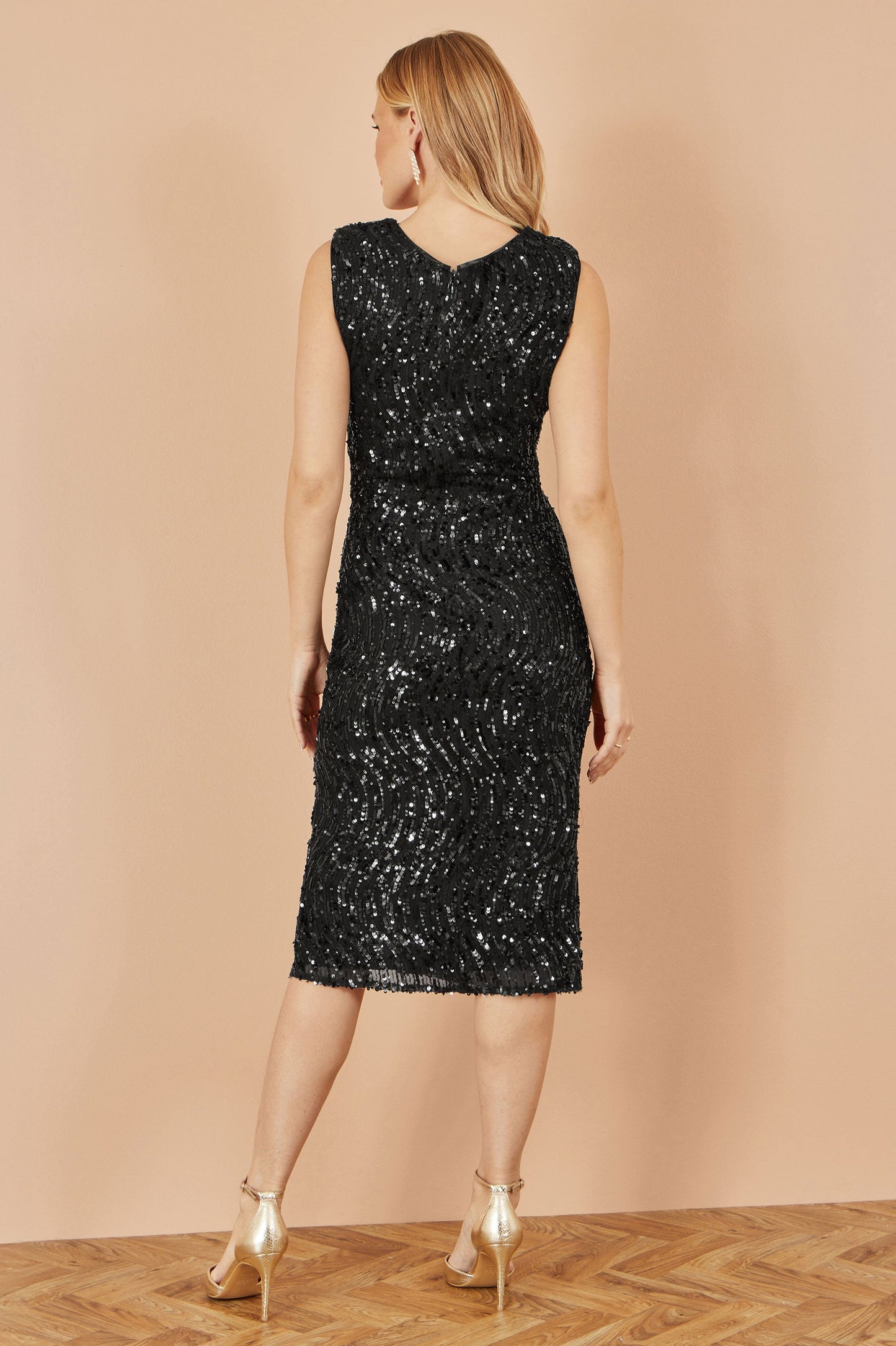 Woman wearing a black sequin dress against a beige wall.