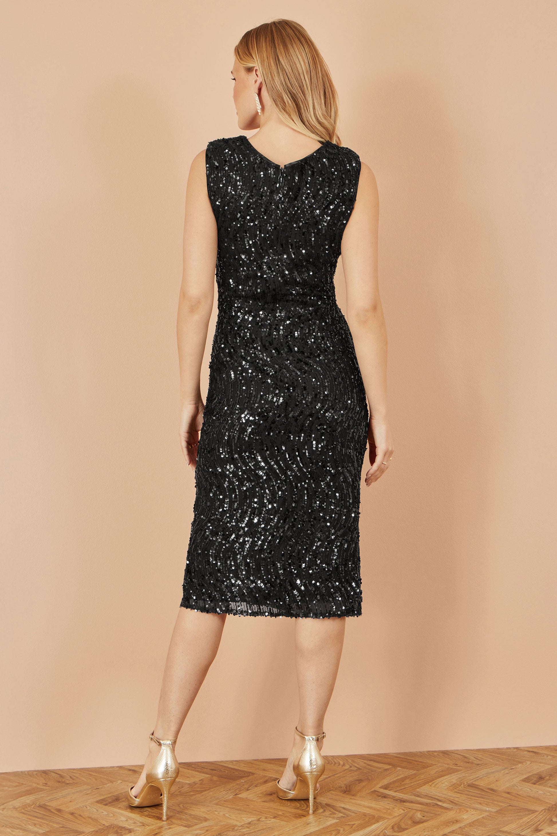 Woman wearing a black sequin dress against a beige wall.