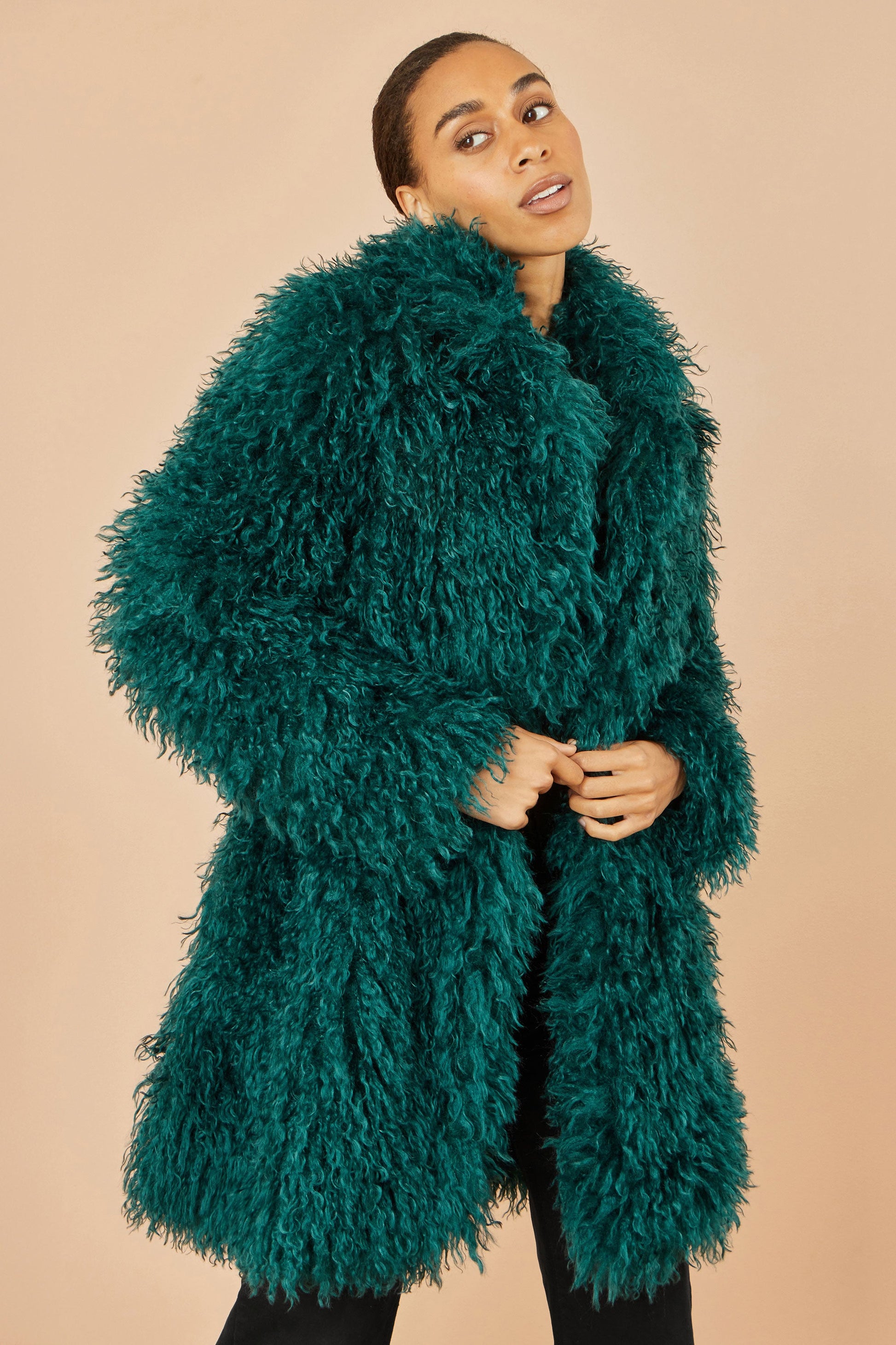 Woman wearing a teal shaggy coat against a beige background