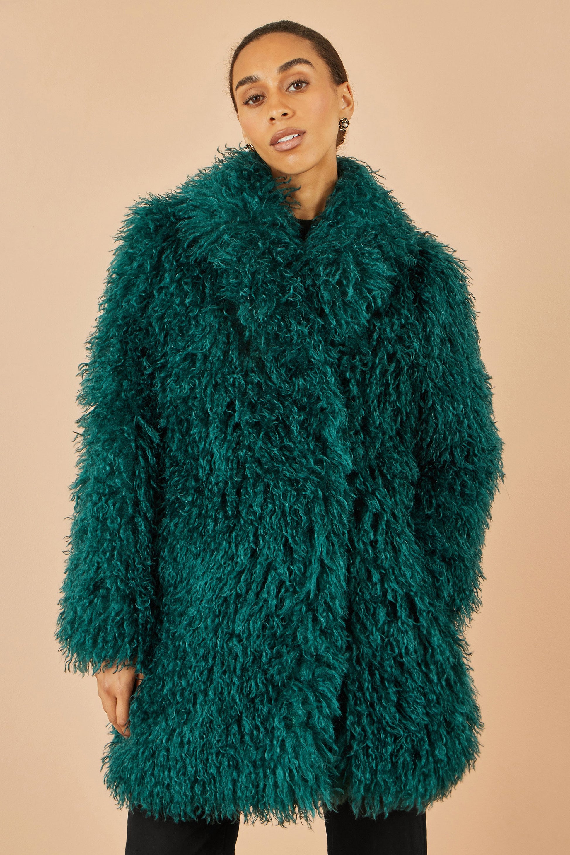Person wearing a teal fluffy coat against a beige background