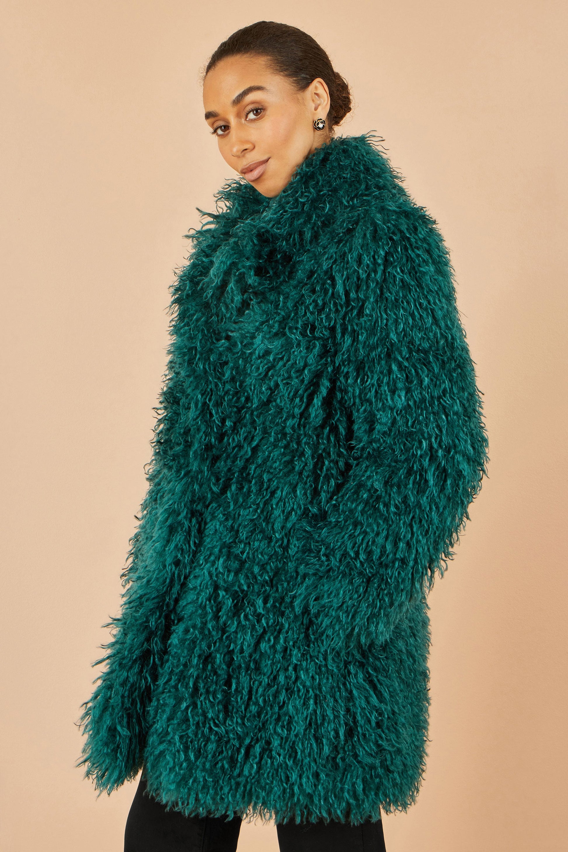 Woman wearing a teal shaggy coat against a beige background