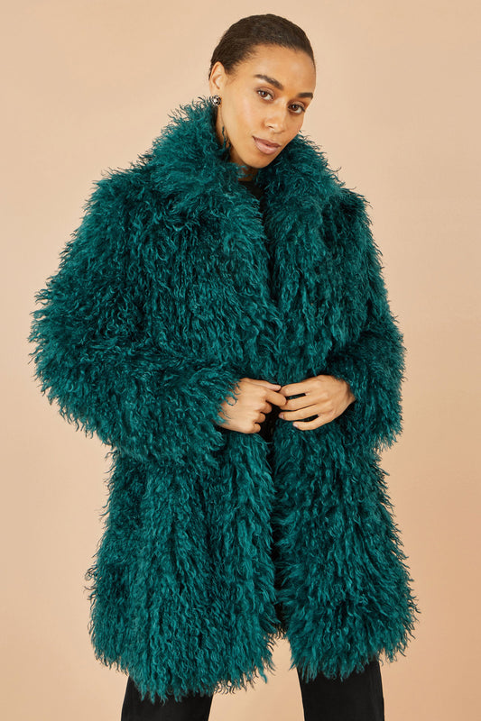 Woman wearing a teal fur coat against a beige background