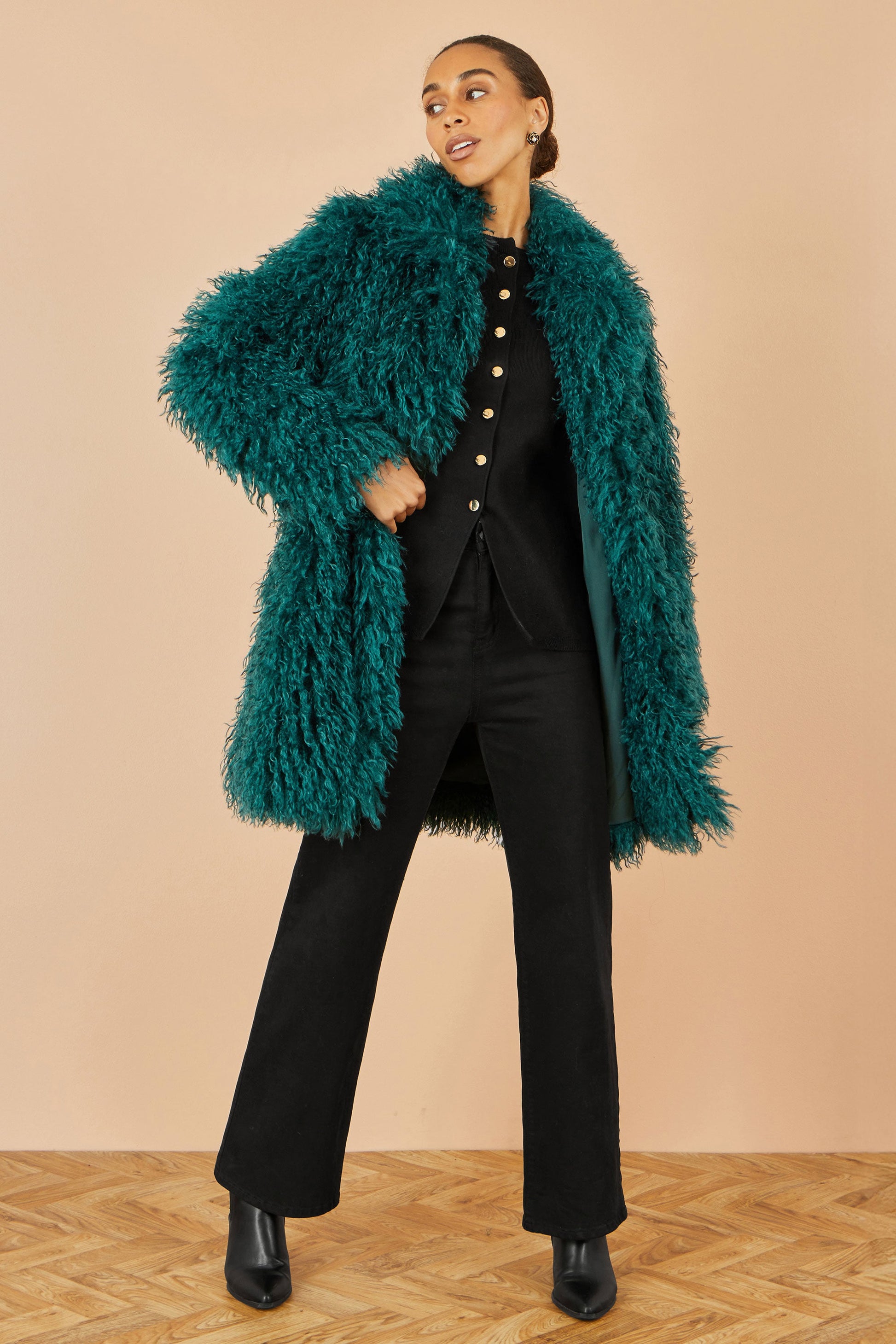 Person wearing a teal fluffy coat over a black outfit on a beige background