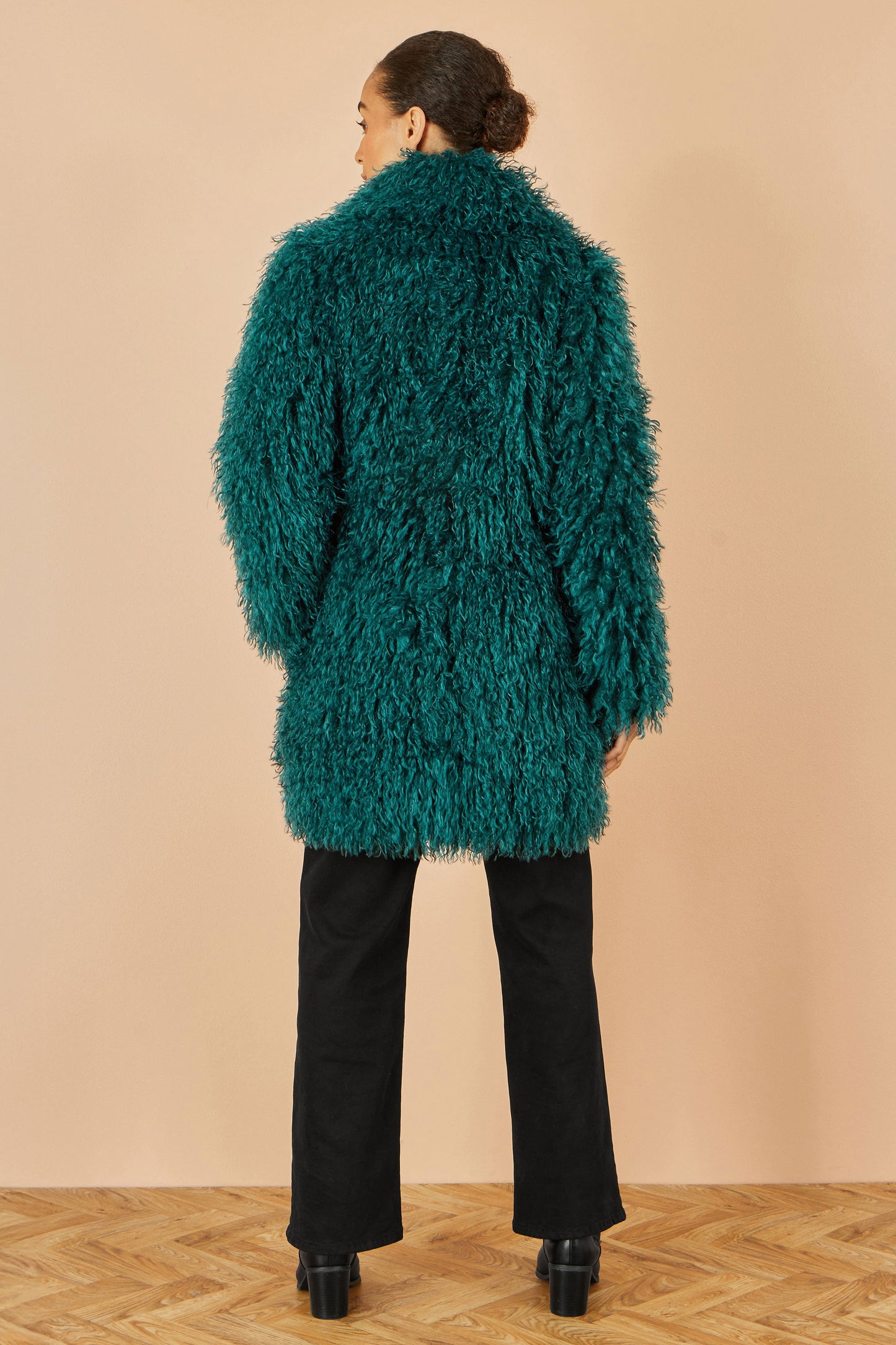 Person wearing a teal fluffy coat against a beige background