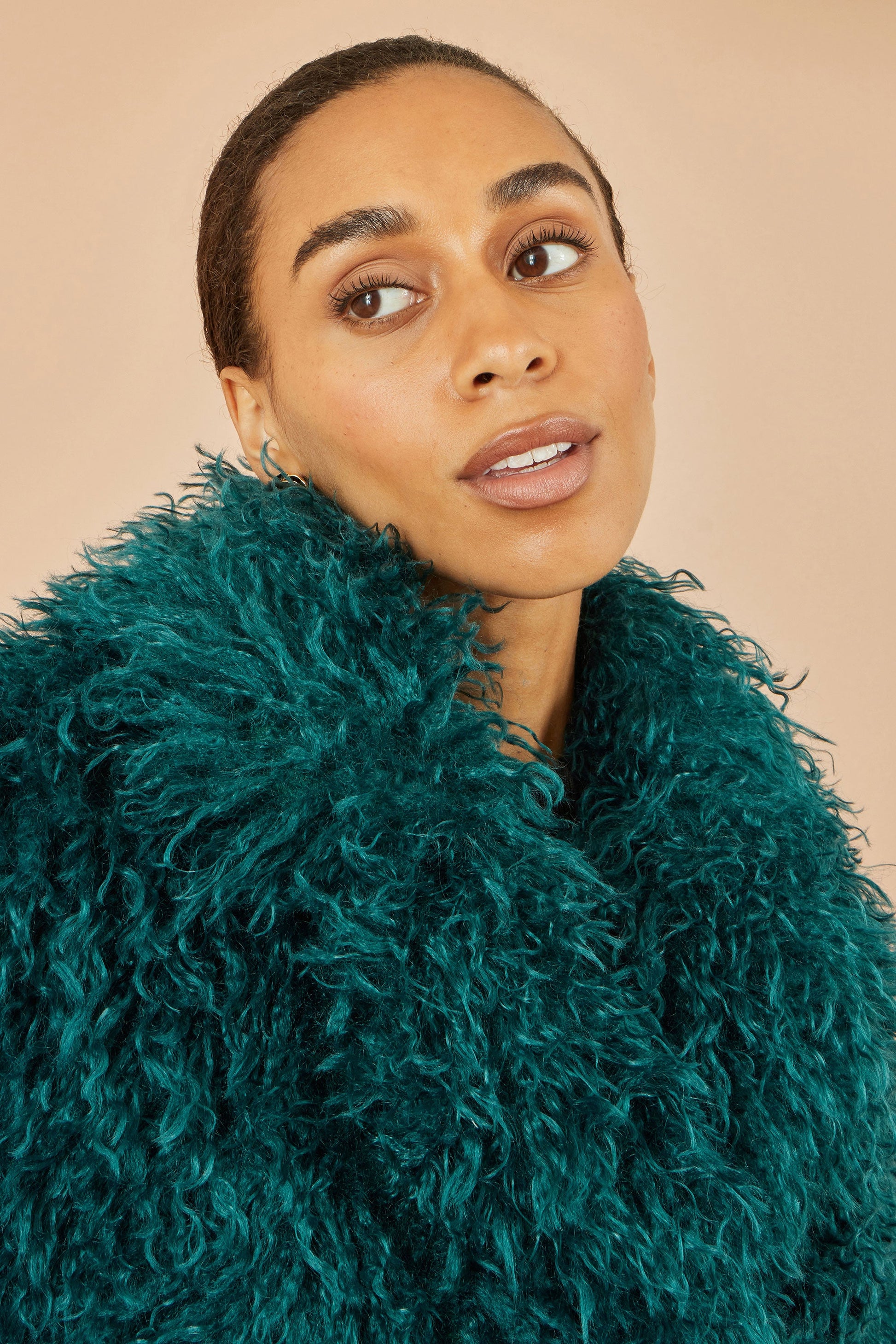 Woman wearing a teal fur coat against a beige background