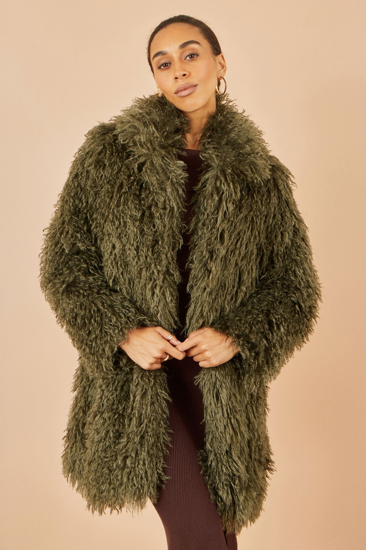Woman wearing a green fluffy coat against a beige background