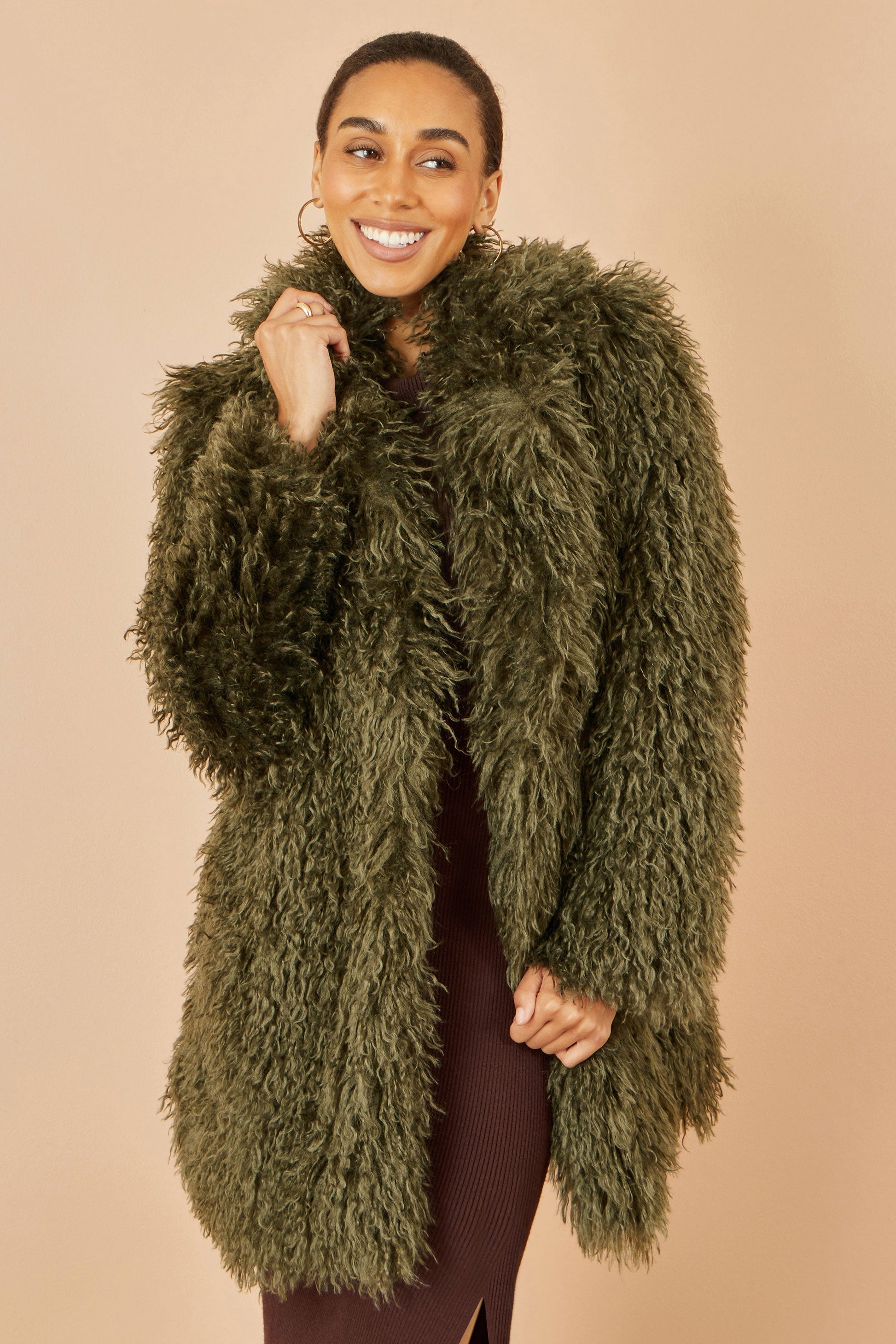 Woman wearing a green fluffy coat against a beige background