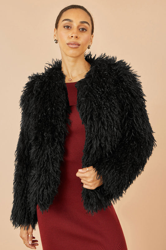 Woman wearing a black fluffy jacket over a red dress on a beige background