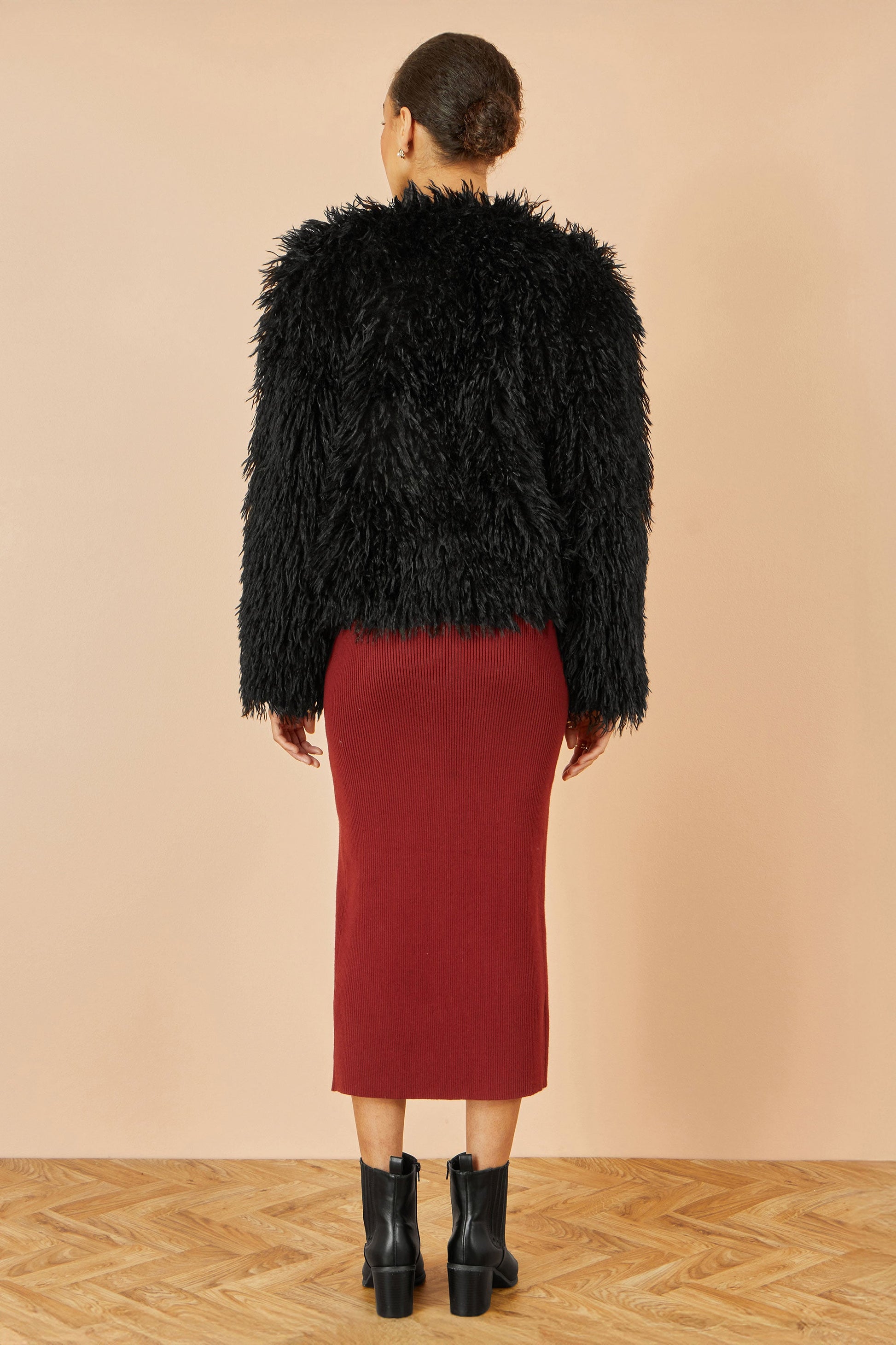 Person wearing a black fluffy jacket and red skirt on a beige background