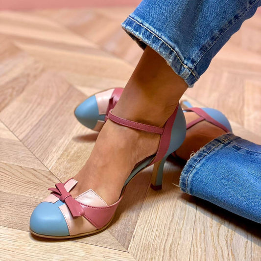 Colorful high-heeled shoes with a bow detail worn with blue jeans on a wooden floor.