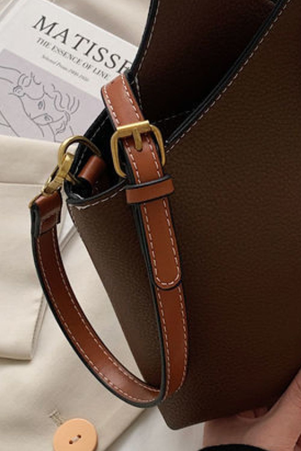 Brown leather handbag with a gold buckle on a light background