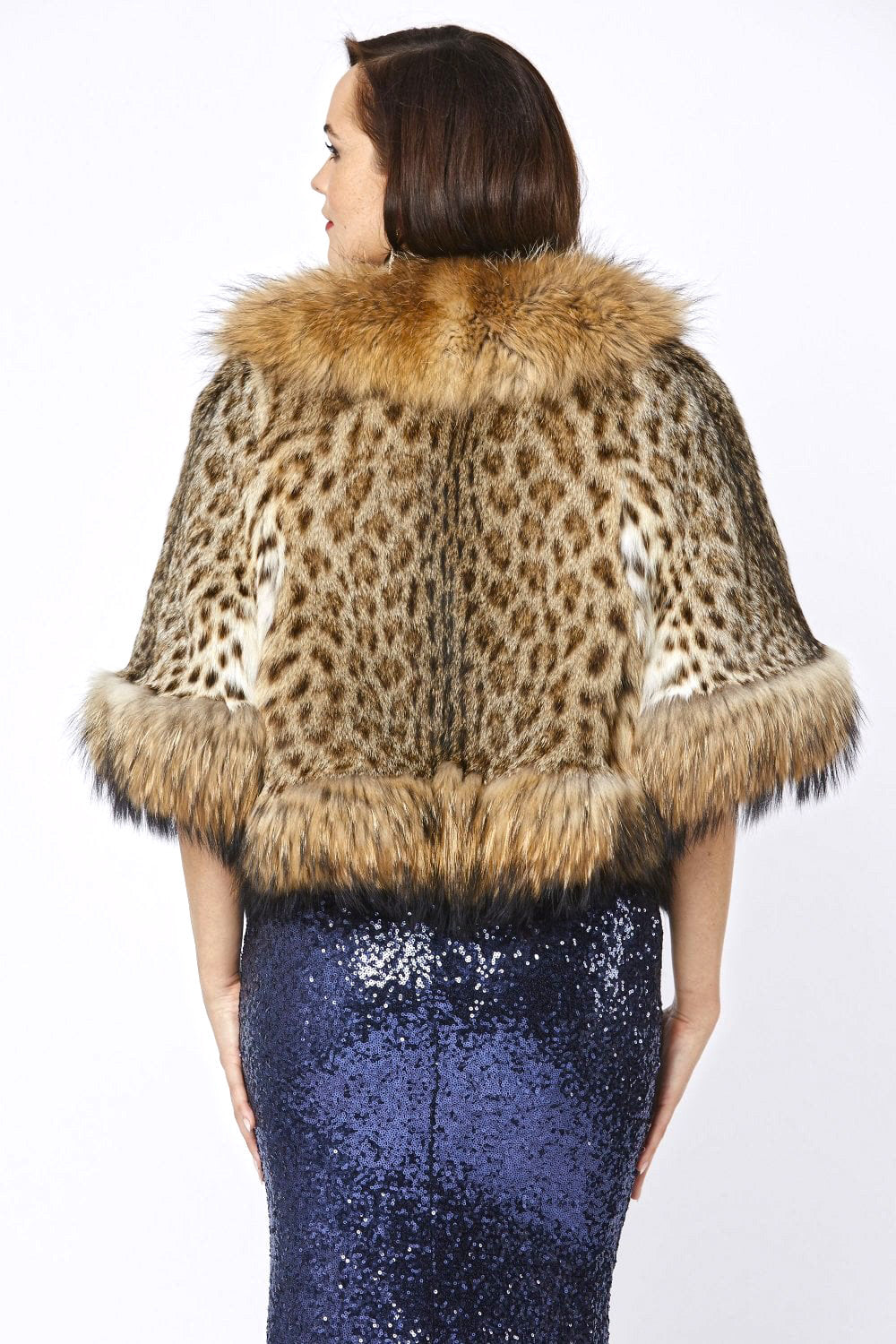 Woman wearing a leopard print cape with fur trim on a white background