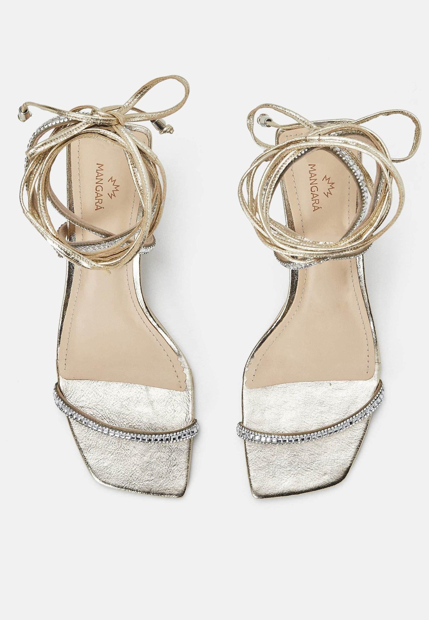 Pair of gold strappy sandals with white lace trim on a light gray background