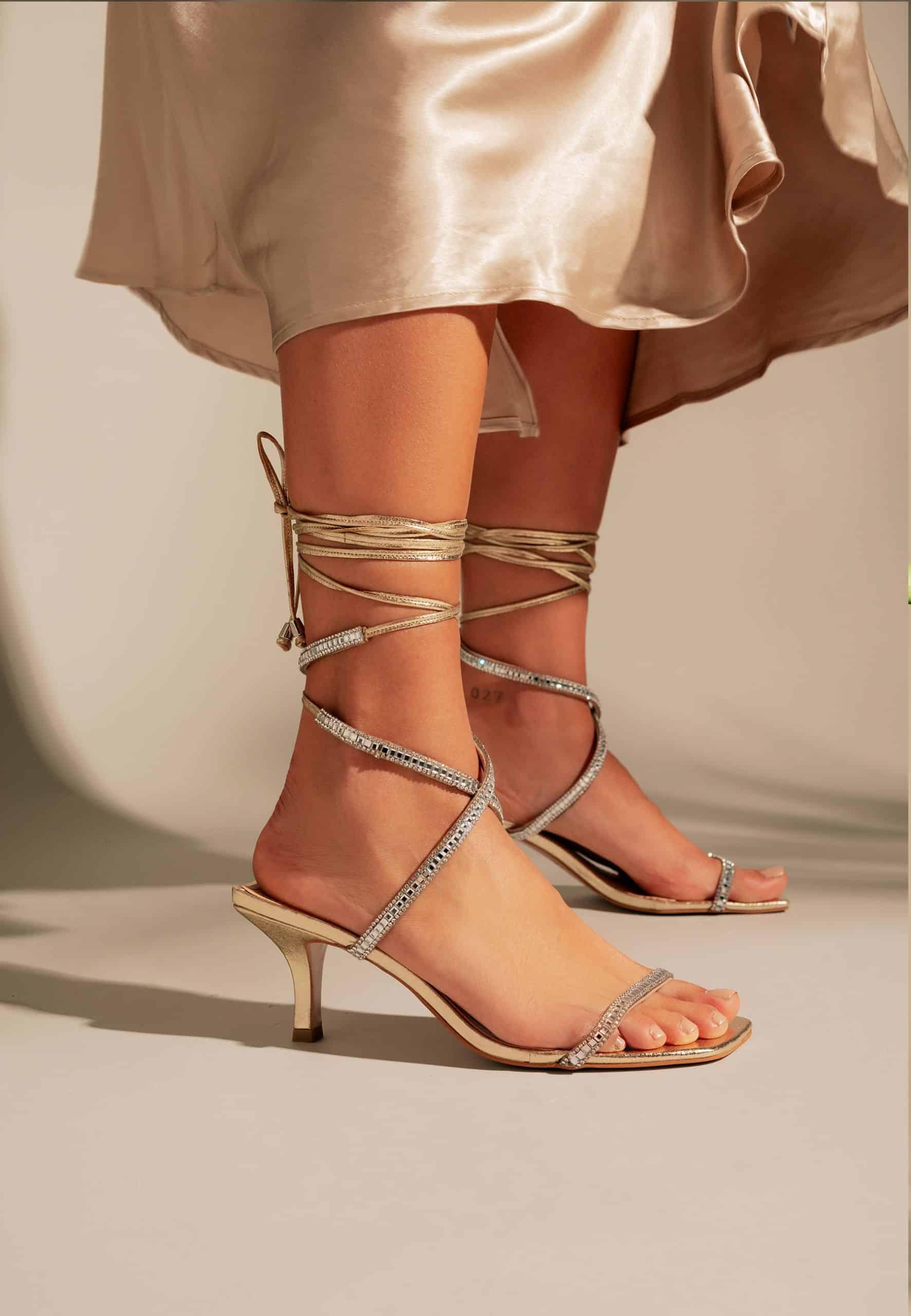 Beige high-heeled sandals with strappy design worn by a person in a light-colored dress.