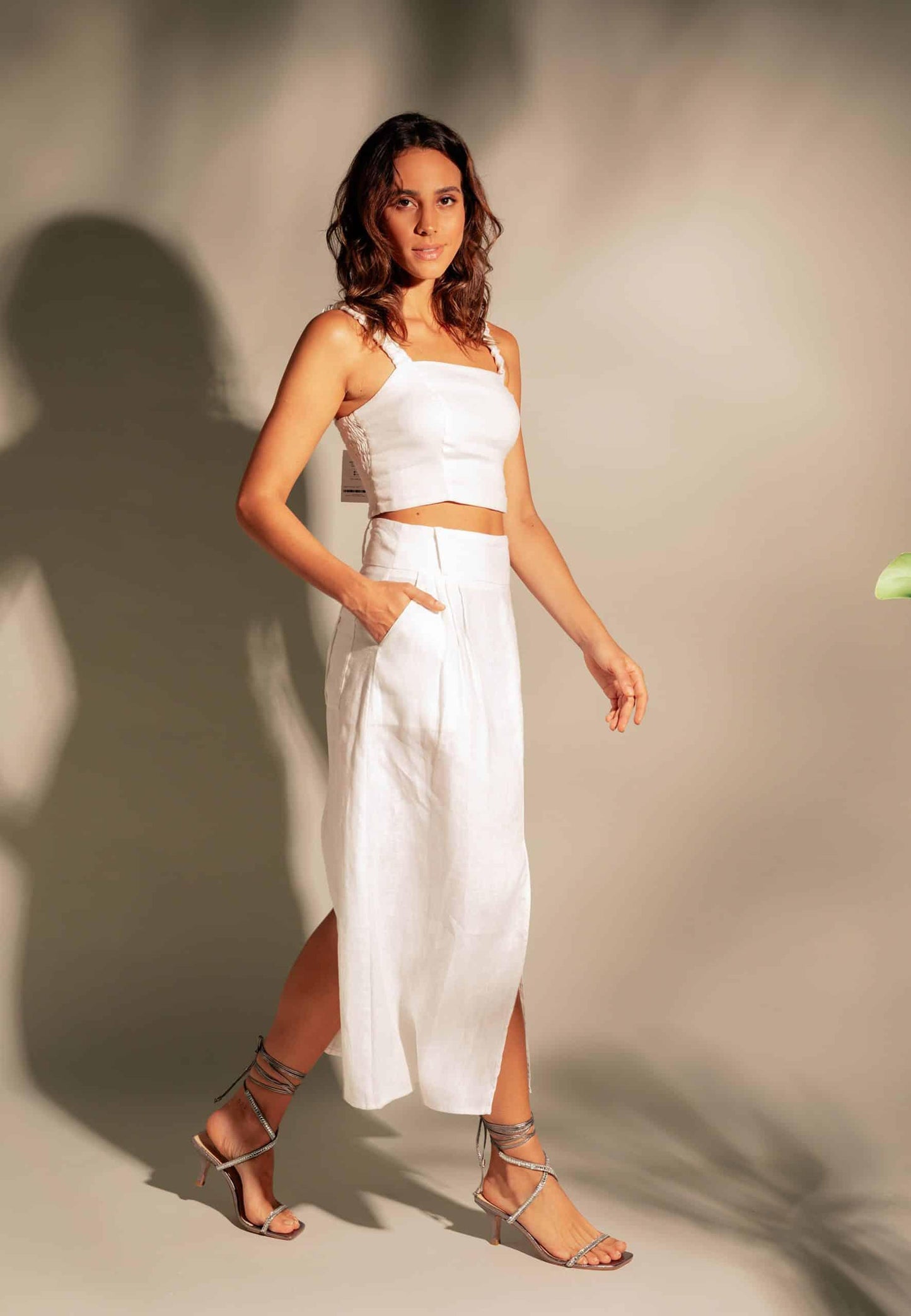 Woman wearing a white outfit with a high slit on a plain background