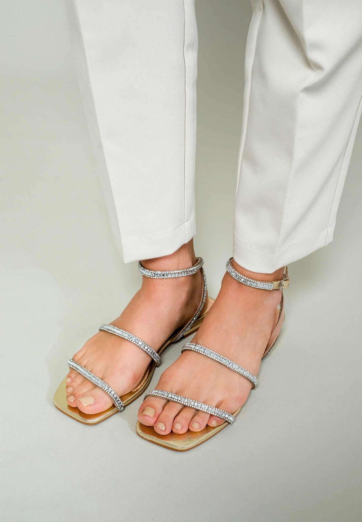 Silver strappy sandals worn with white pants on a light background