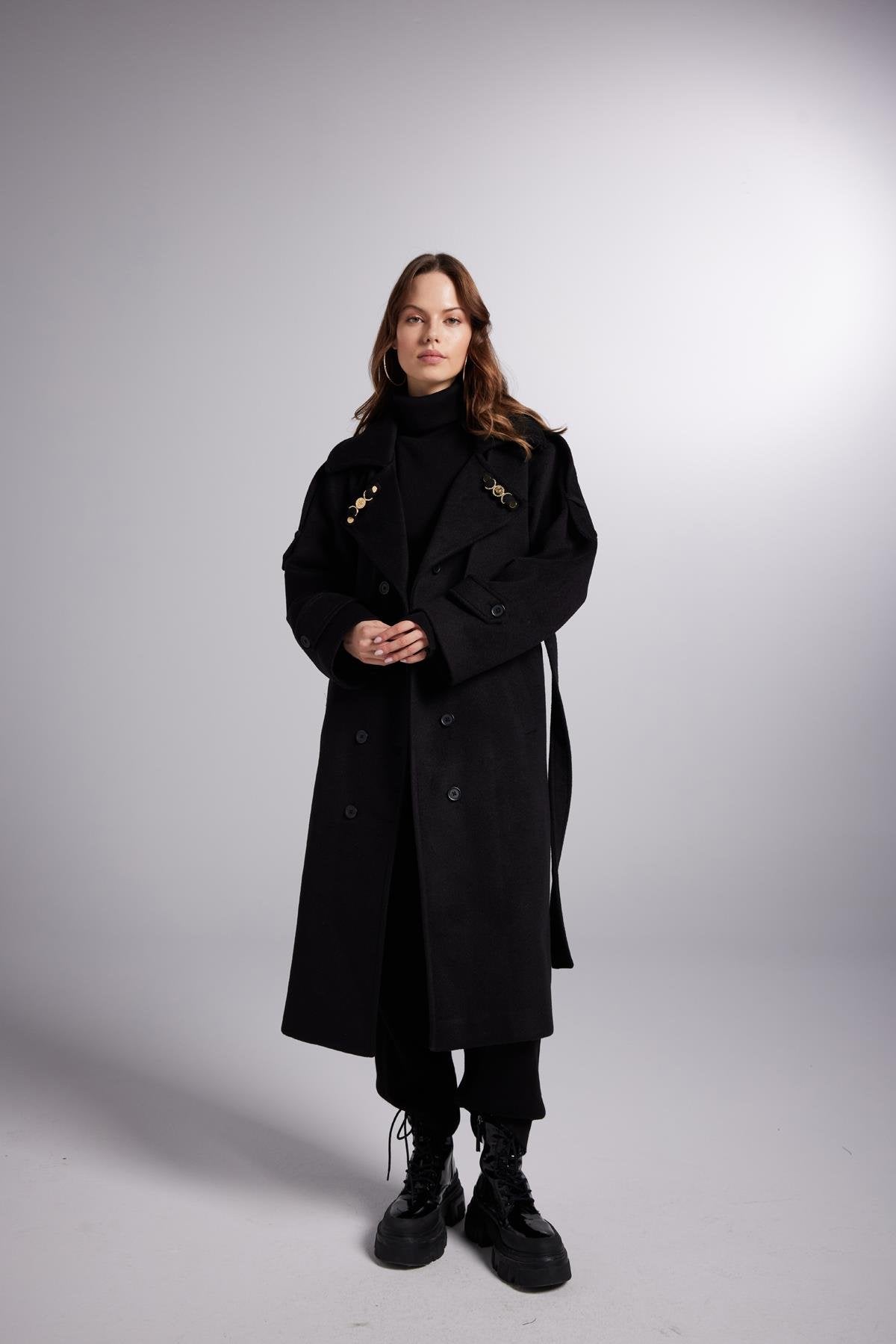 Person wearing a long black coat on a plain background