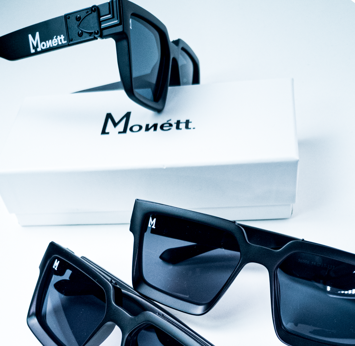 Black sunglasses with 'Monétt' branding on a white background