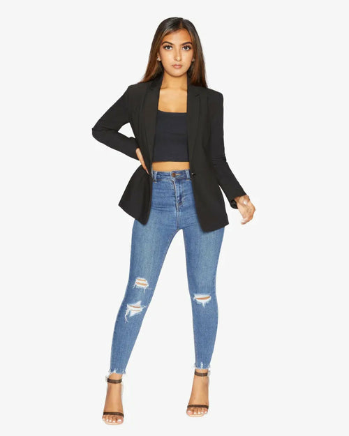 Woman wearing a black blazer, black top, and blue jeans on a white background