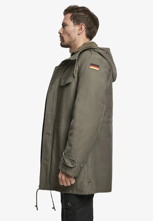 Man wearing a green parka with a German flag patch on a white background