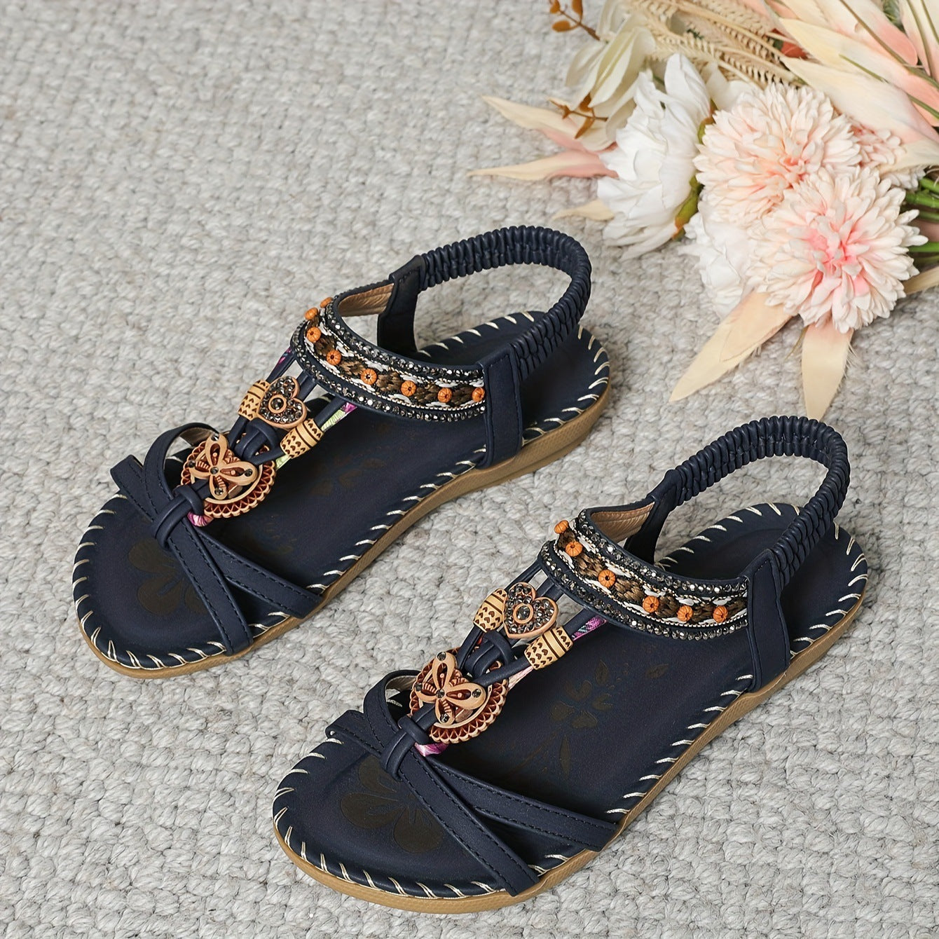 Navy blue sandals with decorative straps on a textured surface with flowers.