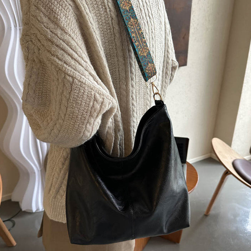 Person wearing a beige sweater with a black handbag over one shoulder indoors.