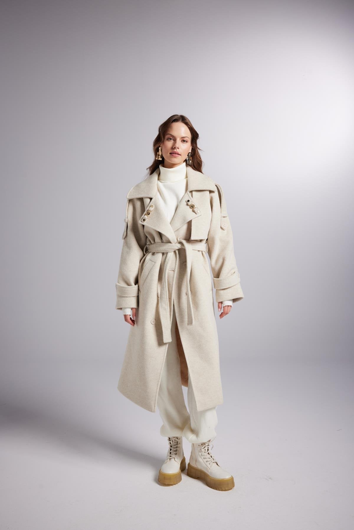 Person wearing a beige trench coat on a gray background
