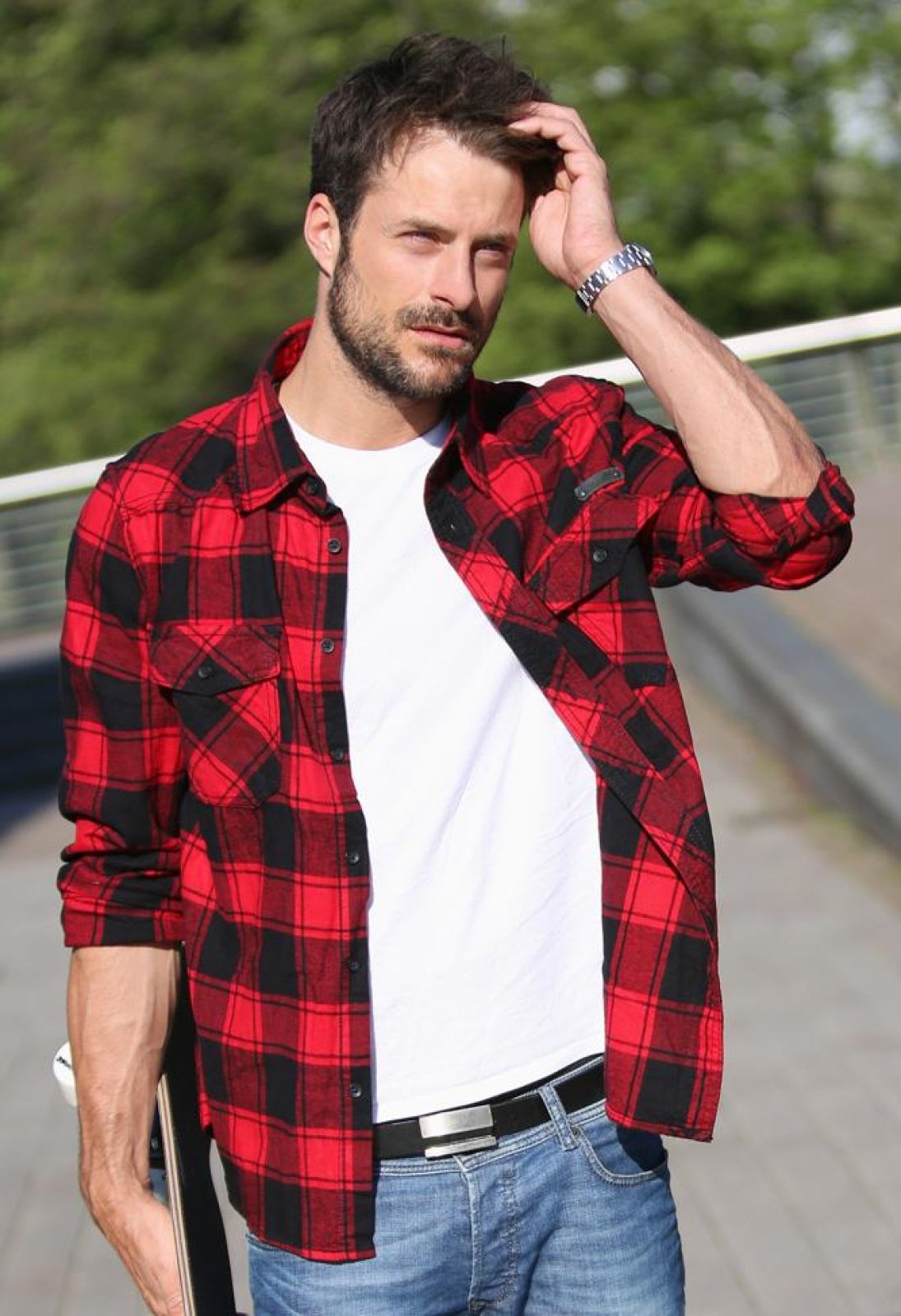 Man wearing a red and black plaid shirt over a white t-shirt, standing outdoors.