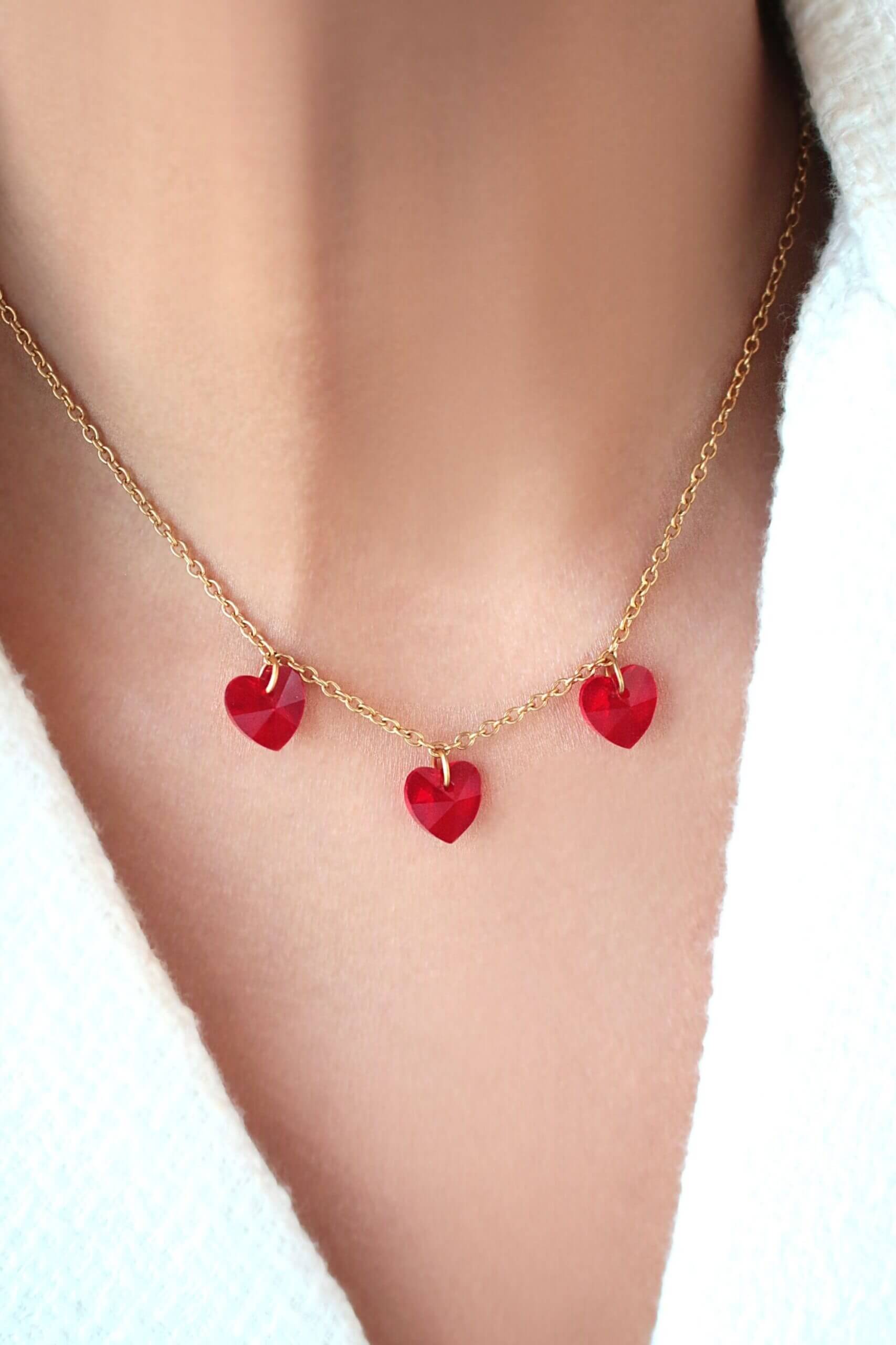 Gold anklet with red heart charms on a person's ankle against a white background