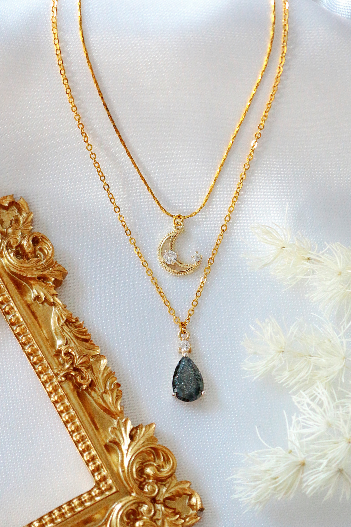 Gold necklace with a teardrop pendant on a white surface with decorative elements.