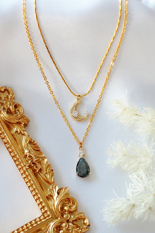 Gold necklace with a teardrop pendant on a white surface with decorative elements.
