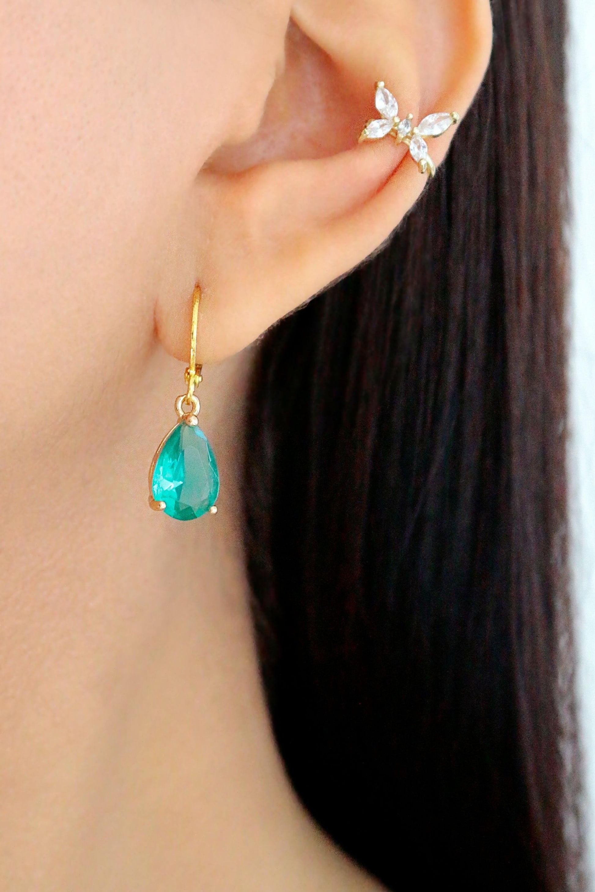Close-up of an ear with a turquoise teardrop earring and gold ear cuff.