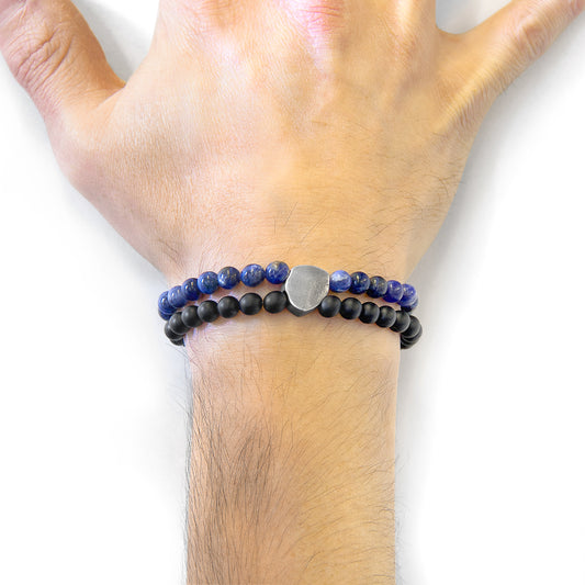 Hand wearing a black and blue beaded bracelet on a white background