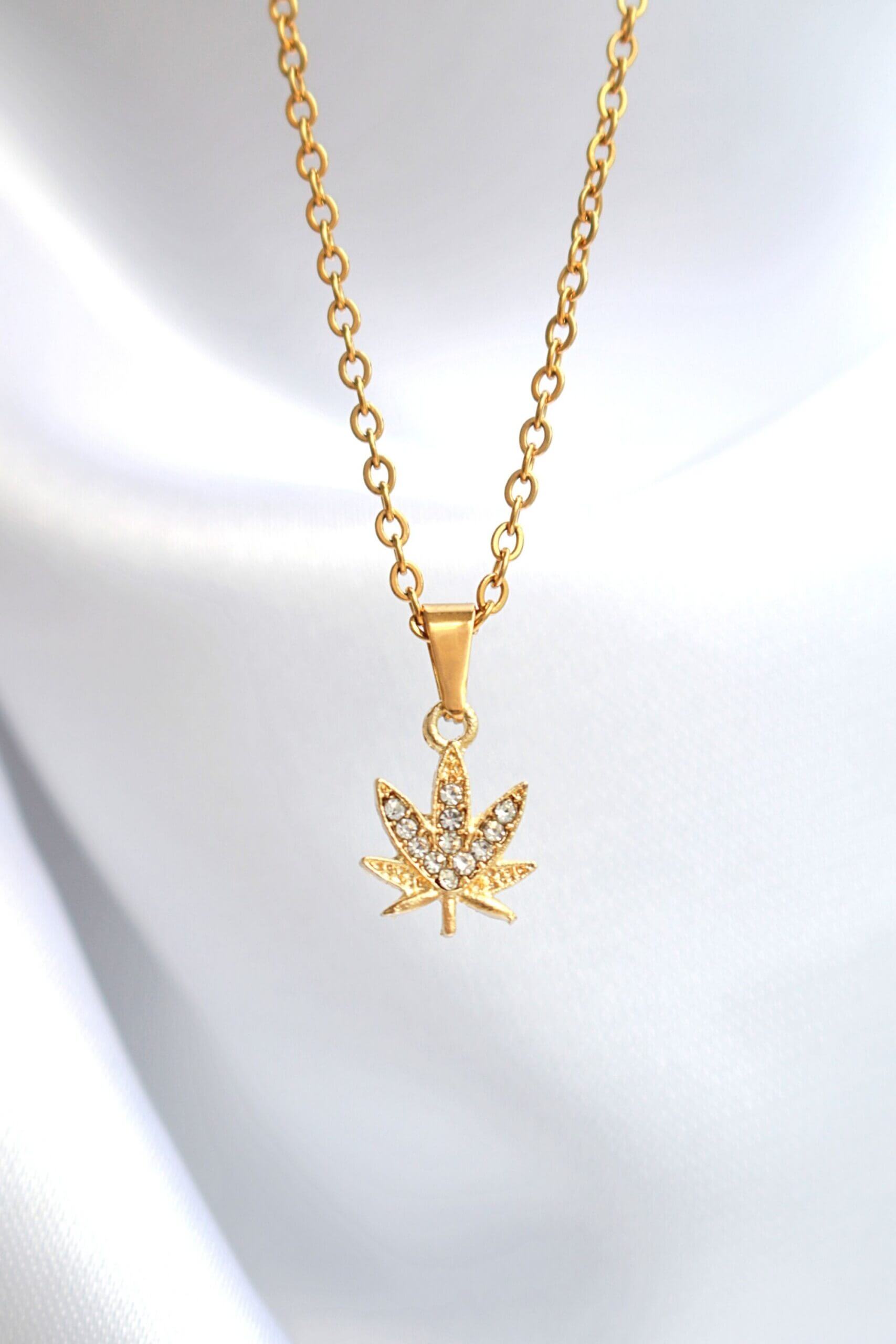 Gold necklace with a leaf-shaped pendant on a light gray background