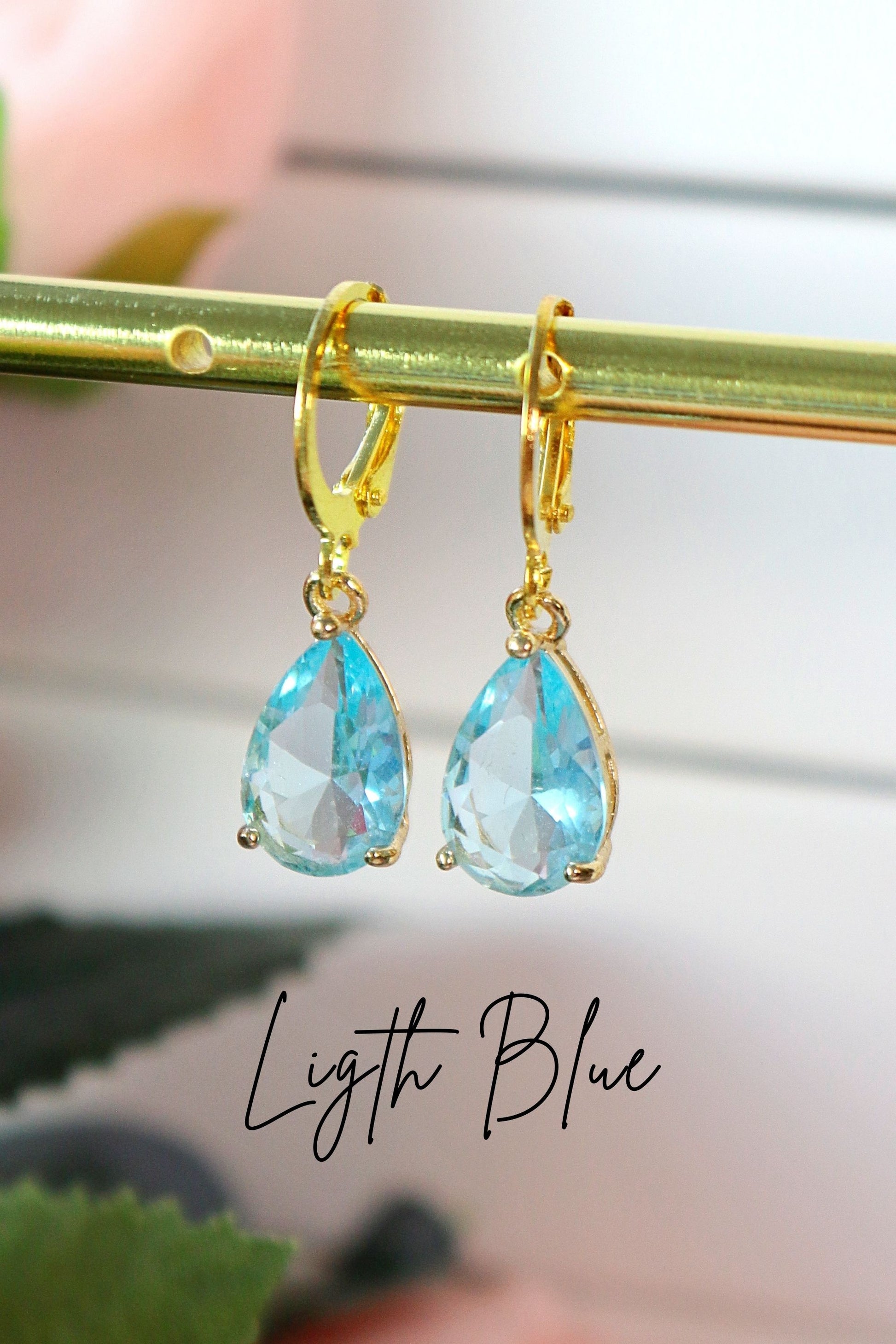 Gold earrings with light blue teardrop-shaped stones on a blurred background